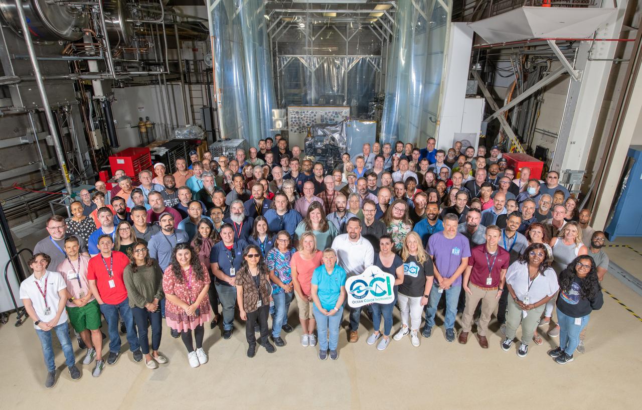 The Ocean Color Instrument (OCI) team pose with OCI and its integrated Earth Shade behind a clean tent curtain. This composite image made of two frames shows the Ocean Color Instrument team standing in front of the flight hardware before the instrument is integrated to the Plankton, Aerosol, Cloud, ocean Ecosystem spacecraft in summer, 2022.  OCI is a highly advanced optical spectrometer that will be used to measure properties of light over portions of the electromagnetic spectrum. It will enable continuous measurement of light at finer wavelength resolution than previous NASA satellite sensors, extending key system ocean color data records for climate studies. OCI is PACE's (Plankton, Aerosol, Cloud, ocean Ecosystem) primary sensor built at Goddard Space Flight Center in Greenbelt, MD.