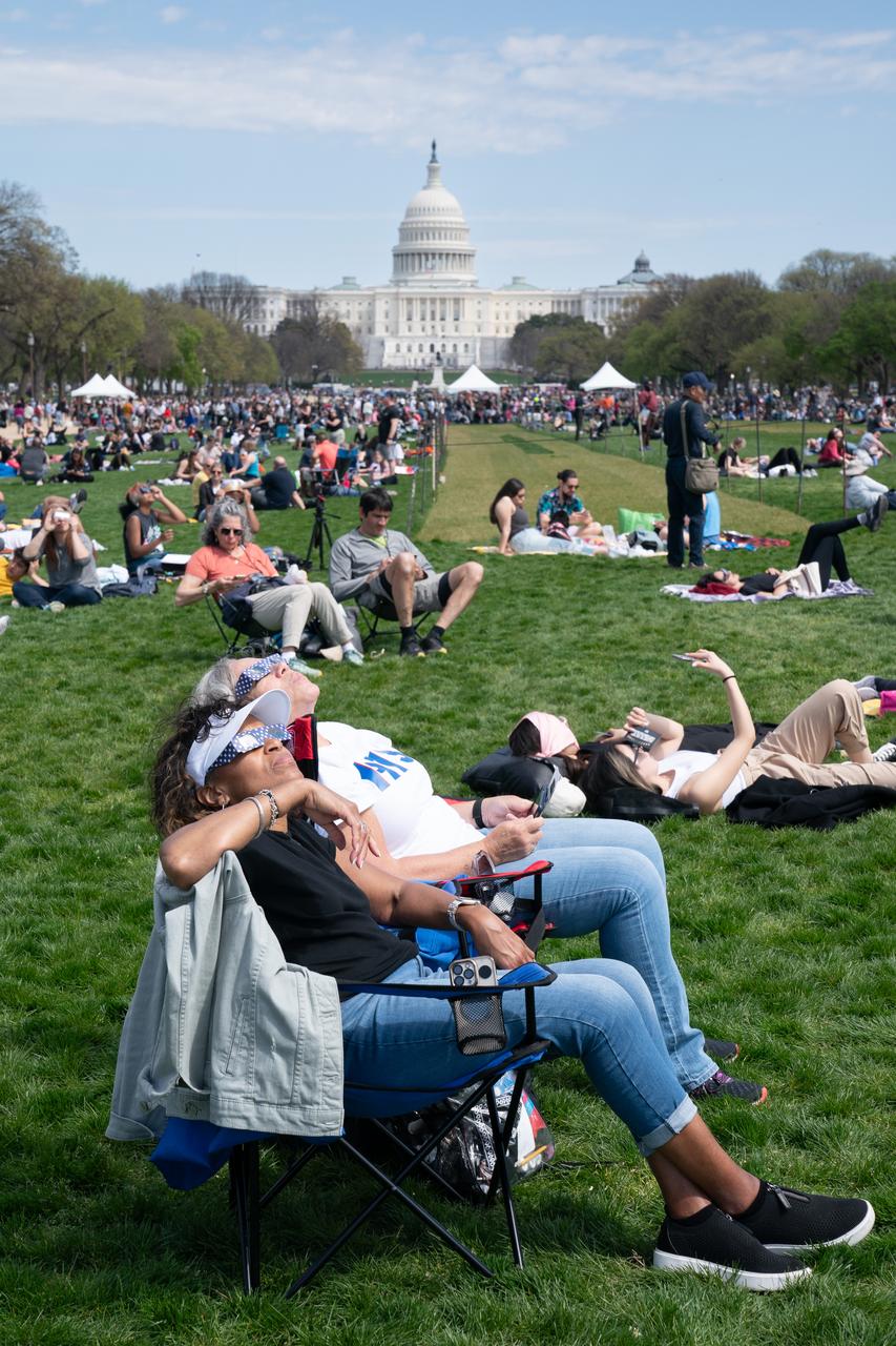 Patricia Jones (front) and Renee Chapman view a partial solar eclipse in Washington, DC, Monday, April 8, 2024. A total solar eclipse swept across a narrow portion of the North American continent from Mexico’s Pacific coast to the Atlantic coast of Newfoundland, Canada. A partial solar eclipse was visible across the entire North American continent along with parts of Central America and Europe. Photo Credit: (NASA/Denny Henry)