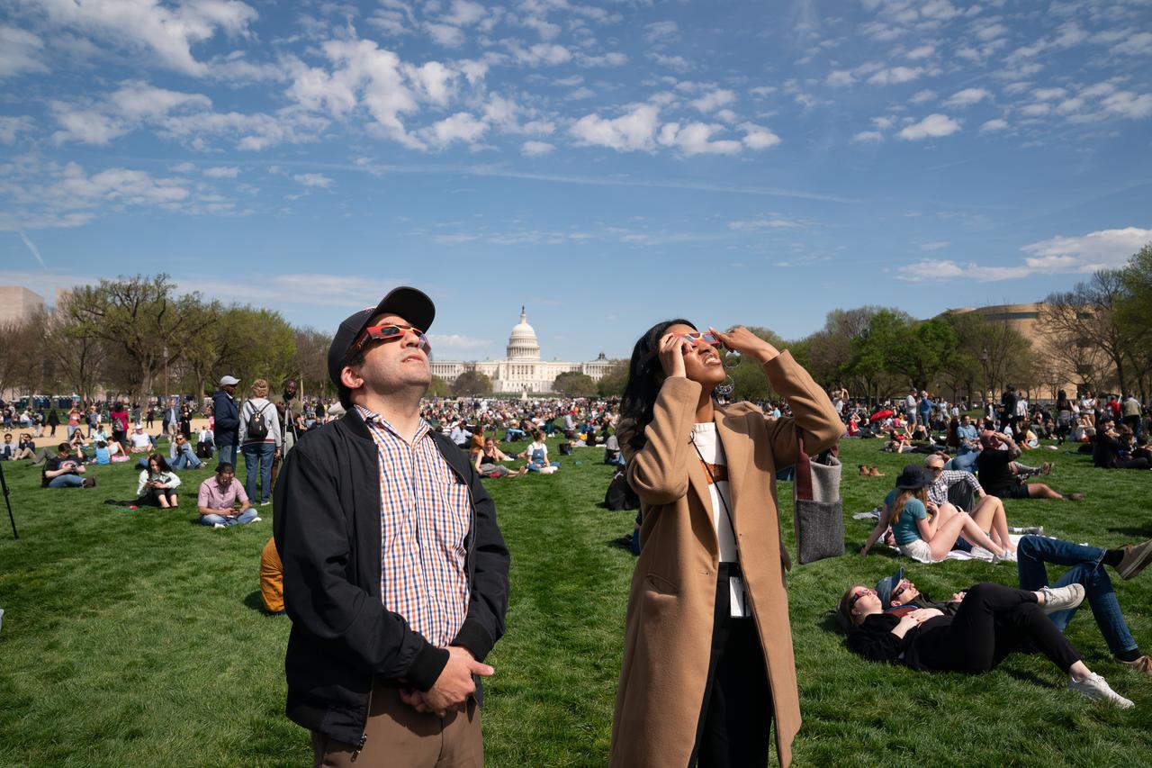 Brian Wolly and Kayla Randall view a partial solar eclipse in Washington, DC, Monday, April 8, 2024. A total solar eclipse swept across a narrow portion of the North American continent from Mexico’s Pacific coast to the Atlantic coast of Newfoundland, Canada. A partial solar eclipse was visible across the entire North American continent along with parts of Central America and Europe. Photo Credit: (NASA/Denny Henry)