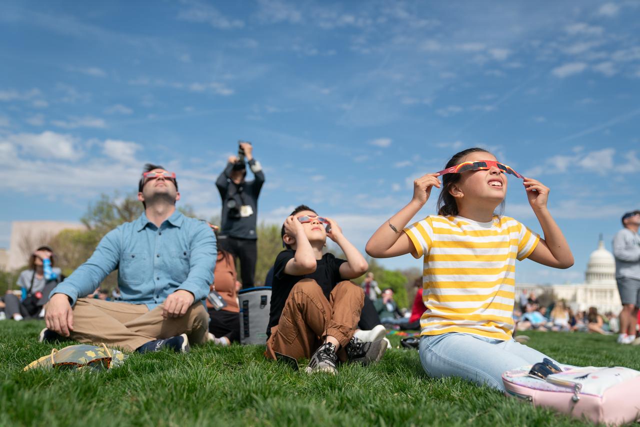 Camila (right), and Cameron (center), with their father Cameron Dyal view a partial solar eclipse in Washington, DC, Monday, April 8, 2024. A total solar eclipse swept across a narrow portion of the North American continent from Mexico’s Pacific coast to the Atlantic coast of Newfoundland, Canada. A partial solar eclipse was visible across the entire North American continent along with parts of Central America and Europe. Photo Credit: (NASA/Denny Henry)