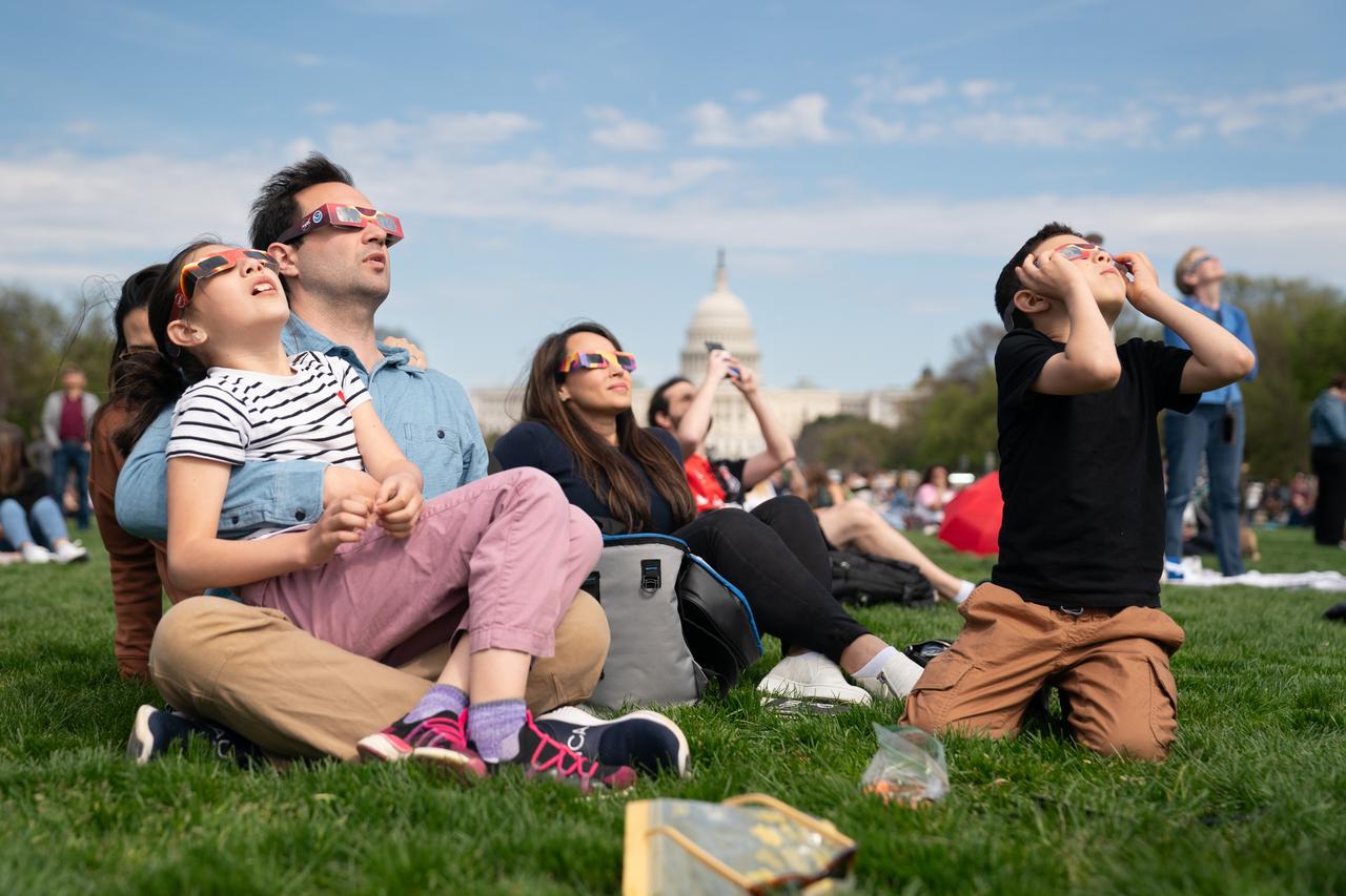 (L-R) Miranda (9) and Cameron Dyal, Yudi Lewis, and Cameron Dyal (7) view a partial solar eclipse in Washington, DC, Monday, April 8, 2024. A total solar eclipse swept across a narrow portion of the North American continent from Mexico’s Pacific coast to the Atlantic coast of Newfoundland, Canada. A partial solar eclipse was visible across the entire North American continent along with parts of Central America and Europe. Photo Credit: (NASA/Denny Henry)W