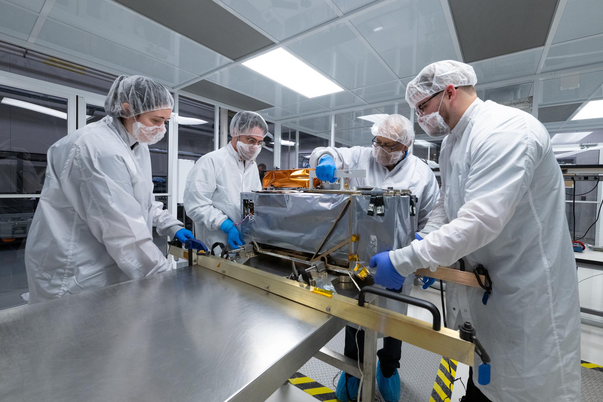 From left, systems engineer Sam Hicks, mechanical engineer Mitchell Hamann, quality engineer Luis Mendez, and technician Lucas Keim lift the Lunar Environment Monitoring Station (LEMS) instrument during testing at the Space Science Center at Morehead State University in Morehead, KY on May 28, 2026. Morehead State University provided LEMS’ telecommunication system and will operate the instrument on the surface. LEMS is a compact, autonomous, and self-sustaining seismometer suite designed to carry out continuous, long-term, monitoring of the lunar seismic environment at the South Polar region. Photo Credit: NASA/Desiree Stover
