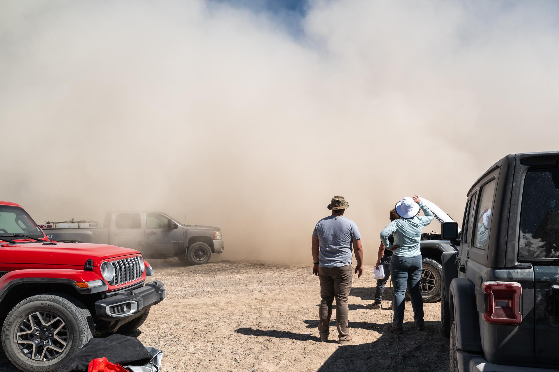 Jason Burt, Lacey Young, and Matt Mullin watch as a helicopter takes off from a test site at Crater Island, June 23, 2026. As the helicopter takes off, it kicks up dust from the ground, reffered to as "roto wash" the dust cloud quickly rises up into a wall of dust before it is blown away by the wind. NASA/Mike Guinto