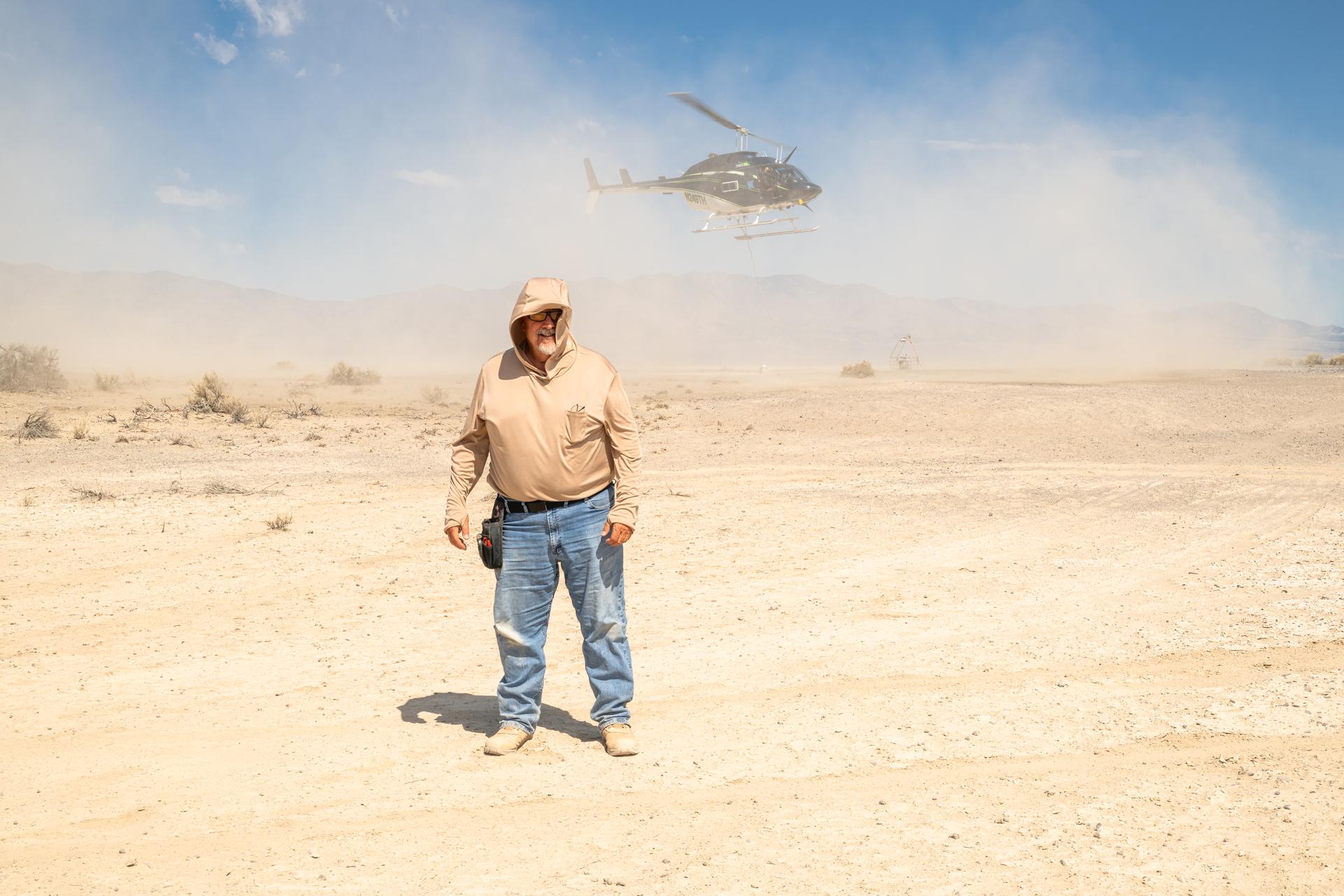 Mike Vitulio, a NASA mechanical integration engineering technician and machinist working on the DAVINCI project poses stands with his back to the helicopter as it takes off to shield himself from the roto-wash at Crater Island, Utah, June 25, 2026. NASA/Mike Guinto