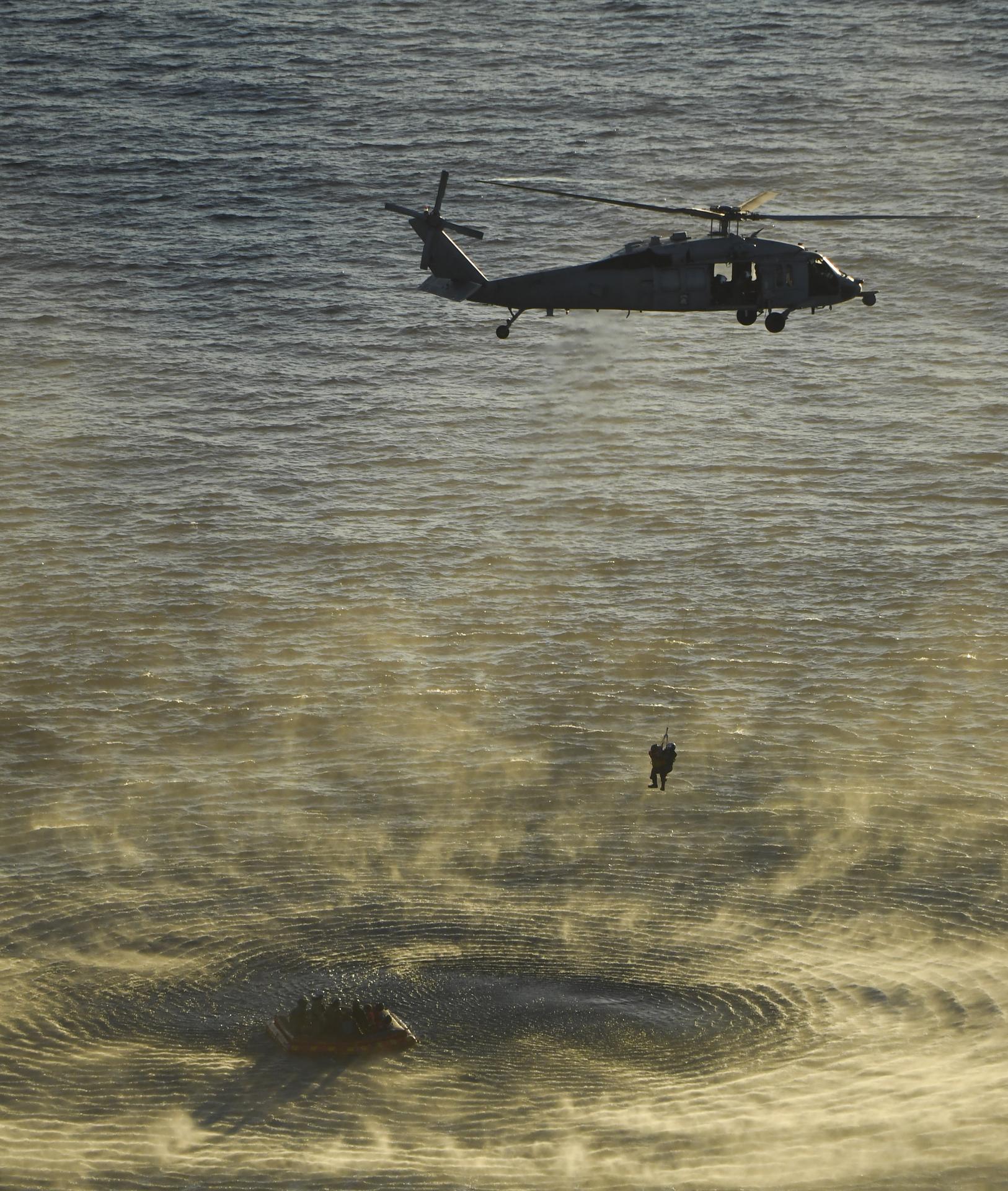 U.S. Navy divers and Artemis II astronauts aboard an inflatable raft are approached by helicopters and lifted away to the...
