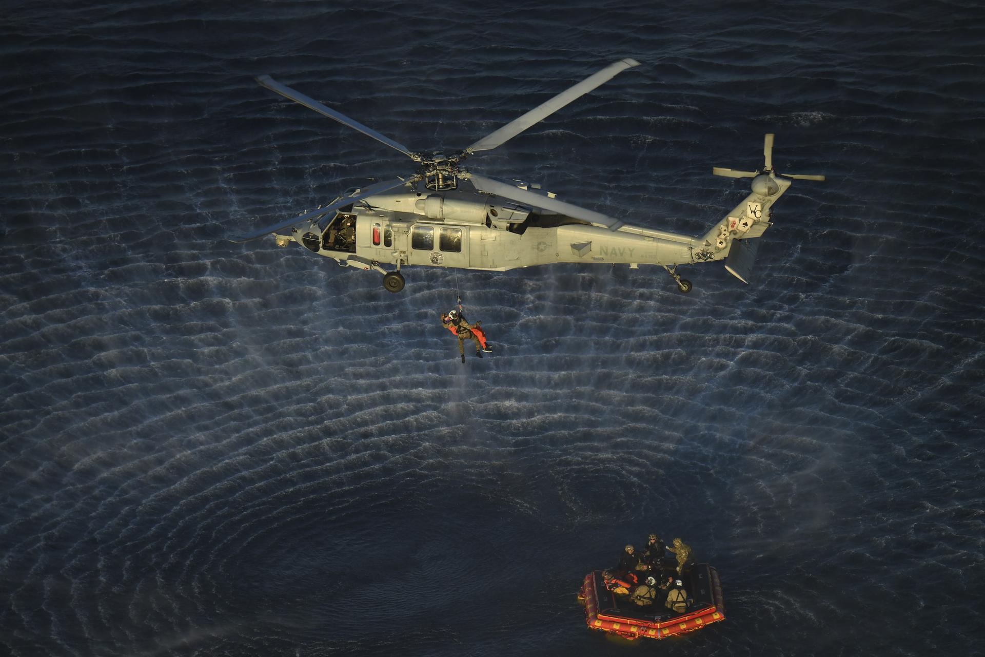 U.S. Navy divers and Artemis II astronauts aboard an inflatable raft are approached by helicopters and lifted away to the...