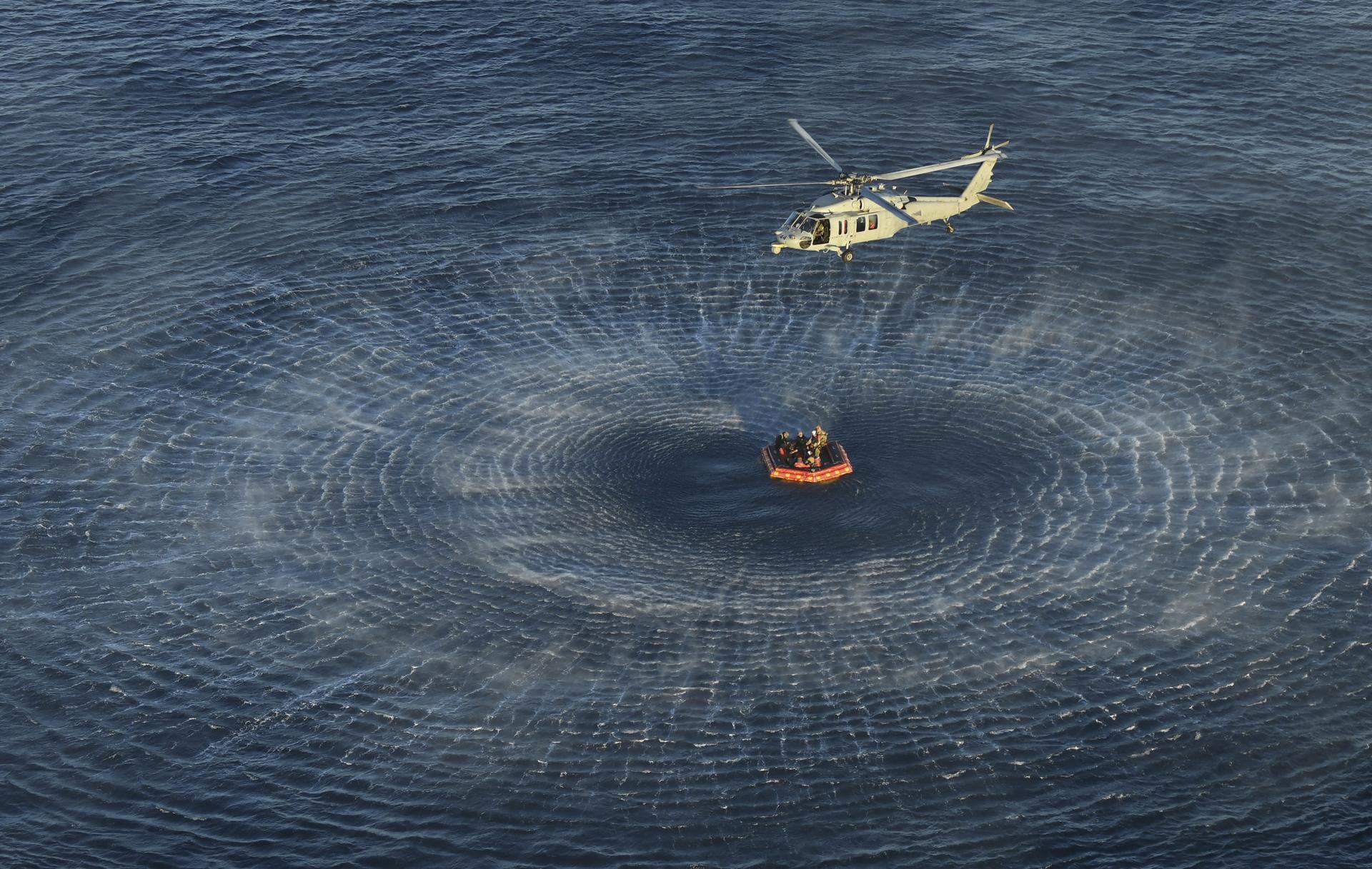 U.S. Navy divers and Artemis II astronauts aboard an inflatable raft are approached by helicopters and lifted away to the...