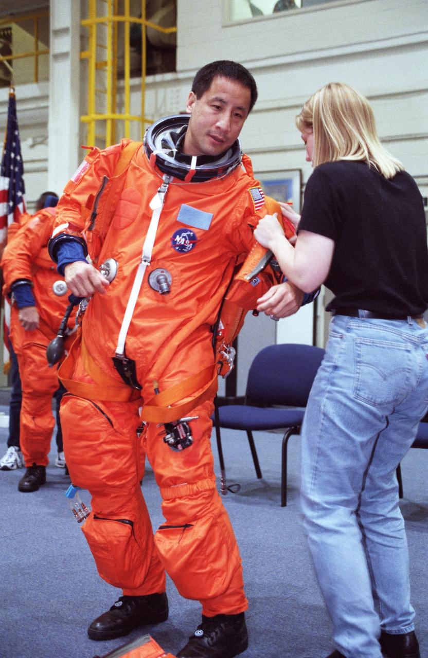 JSC2000-02220 (March 2000) --- Erin Traina, a suit technician for United  Space Alliance (USA), assists astronaut Edward T. Lu with his launch and entry suit prior to a STS-106 training session in the Systems Integration Facility at the Johnson Space Center (JSC).