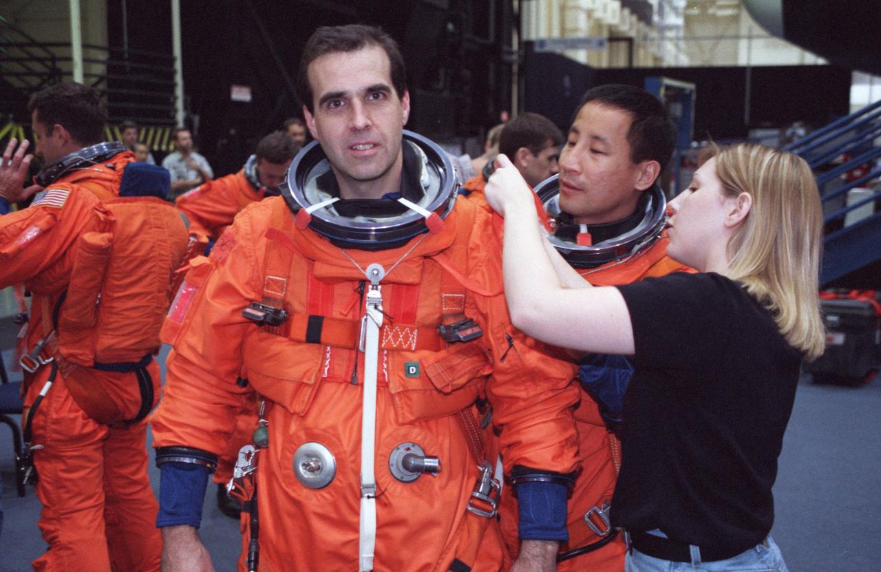 JSC2000-02223 (March 2000) --- Astronaut Edward T. Lu (center foreground) and  United Space Alliance suit technician  Erin Traina assist astronaut Richard A.  Mastracchio with his launch and entry suit.  The two astronauts were about to join their five crewmates for  a simulation of mission activity in the  Systems Integration Facility at the Johnson Space Center (JSC).