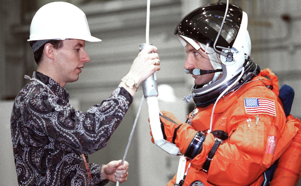 JSC2000-02939 (5 April 2000) ---  David Pogue (left), a crew escape equipment  trainer, briefs astronaut Daniel C. Burbank on the usage of a special device that enables the mission specialist to rappel from a shuttle in trouble on the ground.  A nearby crew-training mockup in the JSC's Systems Integration Facility allowed Burbank and his six crew mates the opportunity to train for procedures to follow in the event of the need to evacuate a distressed shuttle's cabin while on the ground.