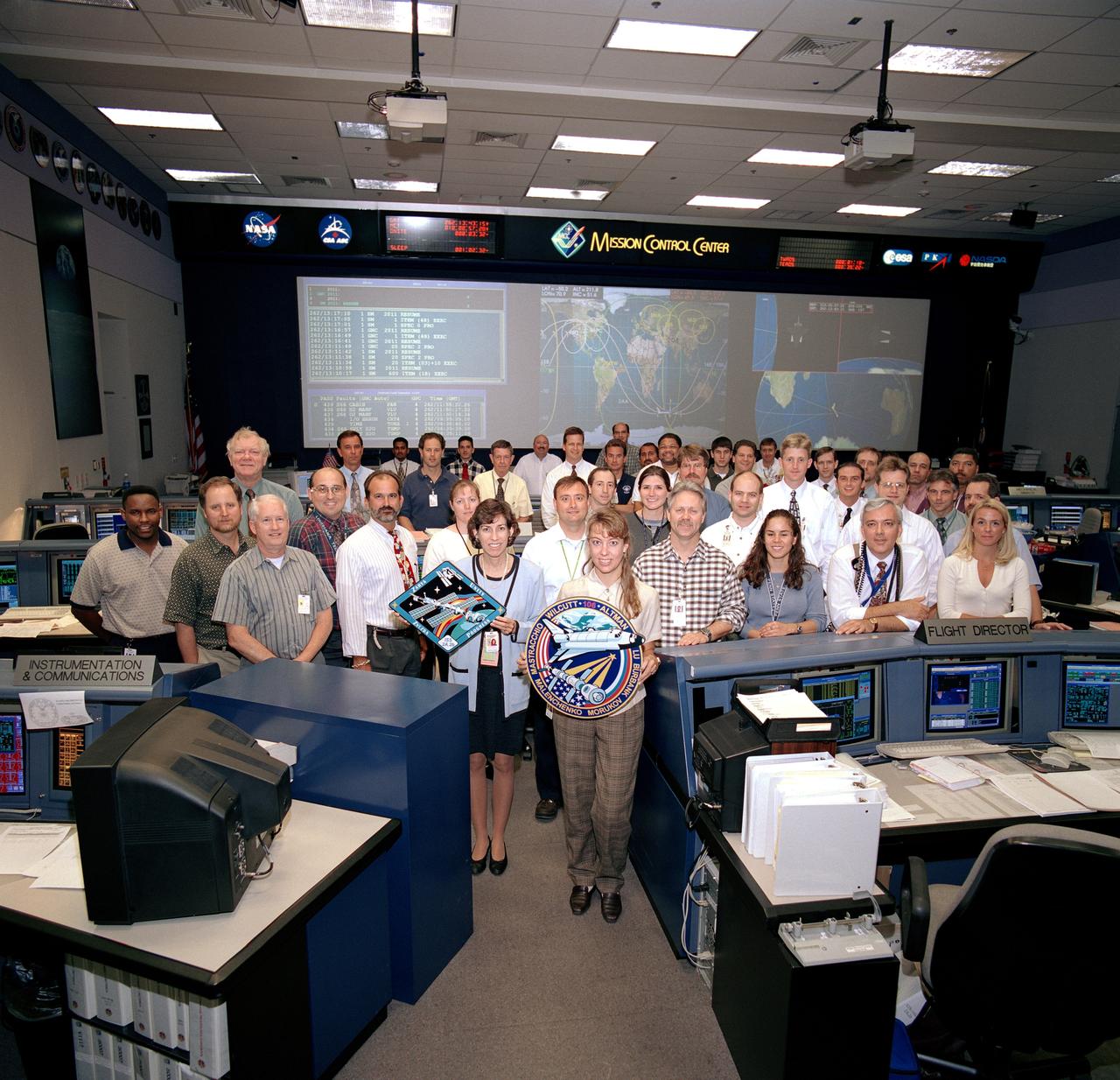 JSC2000-06252 (September 2000) --- Holding logos, flight director Kelly Beck and spacecraft communicator (CAPCOM) Ellen Ochoa pose with the flight control team that supported Orbit 2 during the STS-106 mission.