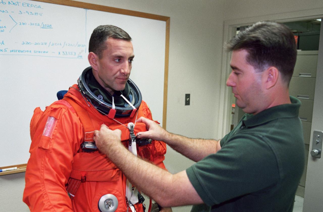 JSC2000-07282 (17 November 2000)--- Astronaut Charles O. Hobaugh, STS-104 pilot, is assisted by suit technician Mike Thompson with a training version of the shuttle launch and entry garment at the Jake Garn Simulation and Training Facility at Johnson Space Center (JSC). Hobaugh, who will join four other astronauts for a June mission with the International Space Station (ISS), shared nearby mockups (out of frame) with his crew mates for a training session dealing with launch and pre-launch issues.