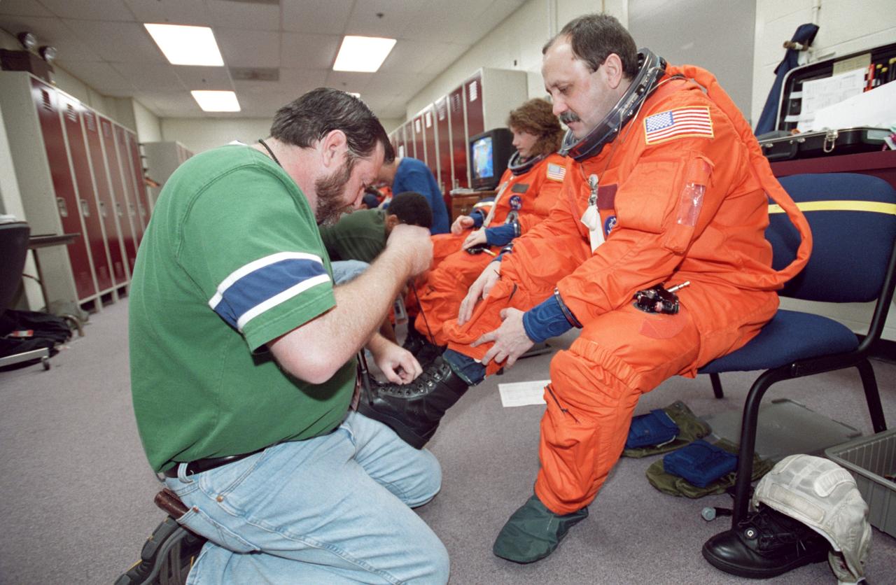 JSC2000-07446 (6 December 2000) --- Suit technician Steve Clendenin helps cosmonaut Yury V. Usachev with his boot straps during an STS-102 training session in the Systems Integration Facility at the Johnson Space Center (JSC).   The Expedition Two commander, along with two astronauts on his crew and the four STS-102 crew members, later simulated procedures for a nominal countdown in the crew compartment trainer (CCT-2) in the high bay area of this facility.
