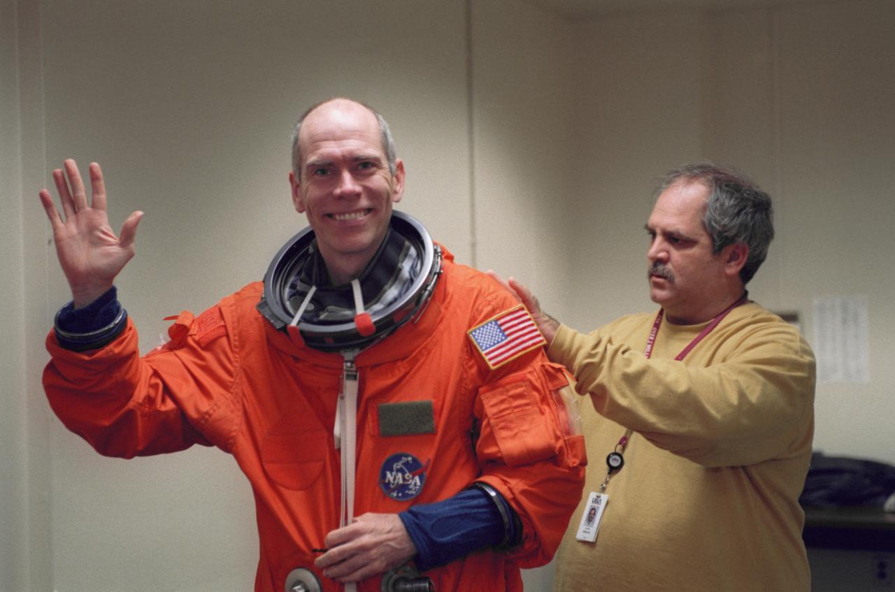JSC2000-07655 (19 December 2000) --- Astronaut Daniel T. Barry, STS-105 mission specialist, dons a training version of the full-pressure launch and entry suit prior to a training session in one of the trainer/mockups (out of frame) in the Jake Garn Simulation and Training Facility at Johnson Space Center (JSC). Barry is assisted by United Space Alliance (USA) suit technician Lloyd Armintor.