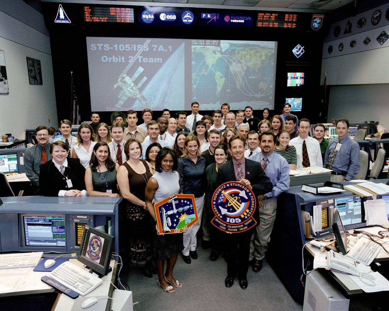 JSC2001-02225 (17 August 2001) --- The members of the STS-105/ISS 7A.1 Orbit 2 team pose for a group portrait in the International Space Station (ISS) flight control room (BFCR) in Houston&#0146;s Mission Control Center (MCC). Orbit 2 flight director Rick LaBrode (front right) holds the STS-105 mission logo, and Astronaut Joan E. Higginbotham, ISS spacecraft communicator (CAPCOM), holds the ISS 7A.1 mission logo.