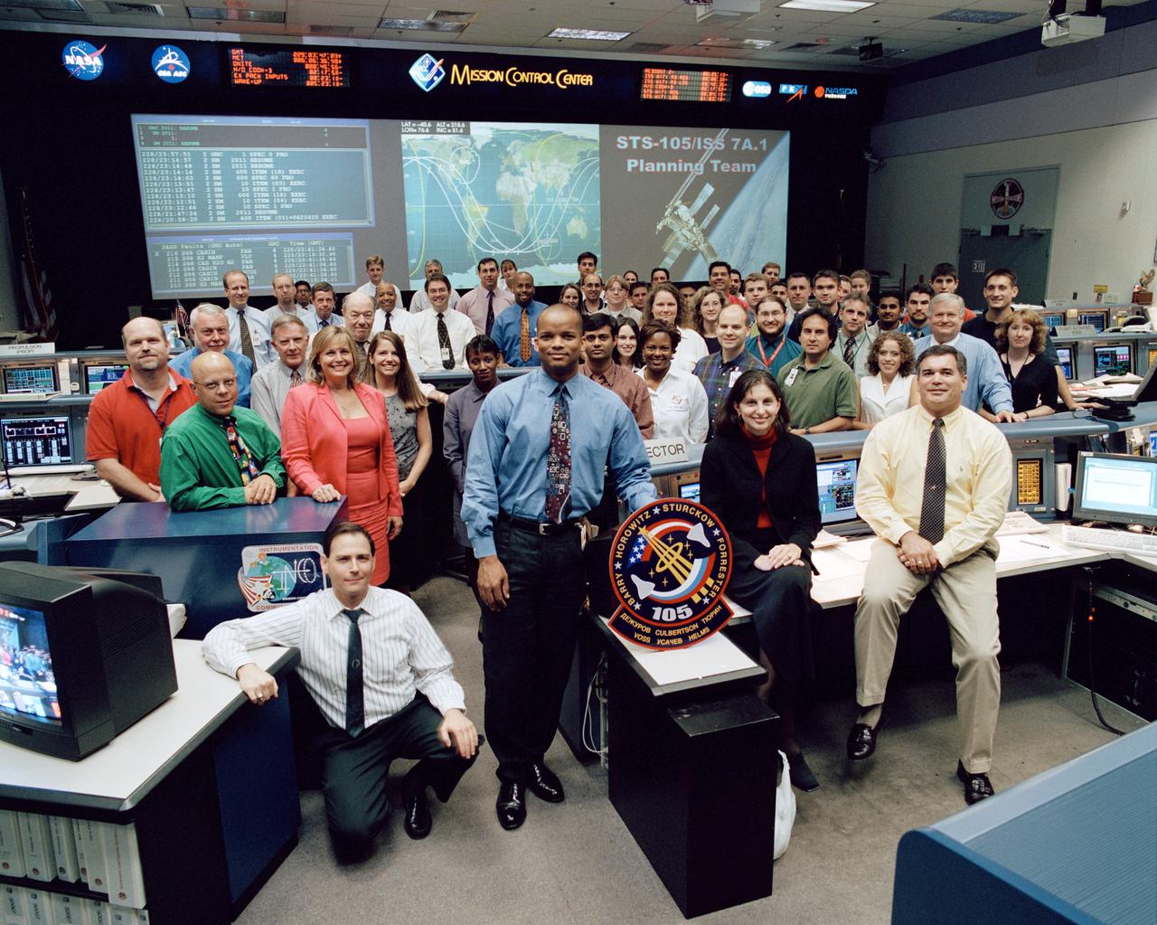 JSC2001-02228 (16 August 2001) --- The members of the STS-105/ISS 7A.1 Planning team pose for a group portrait in the shuttle flight control room (WFCR) in Houston’s Mission Control Center (MCC). Astronaut Robert L. Curbeam, Jr., spacecraft communicator (CAPCOM), stands behind the STS-105 mission logo. Flight director Bryan Austin is visible in the front row on the far right.
