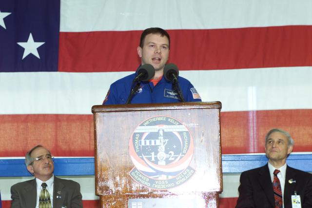 JSC2001-E-08328 (22 March 2001) --- Astronaut James M. Kelly, STS-102 pilot, speaks to a crowd of greeters during a crew return ceremony in Ellington Field's Hangar 990.  Pictured in the background on the dais are Joseph Rothenberg (left), NASA Associate Administrator for Space Flight, and Roy S. Estess, Johnson Space Center Acting Director.