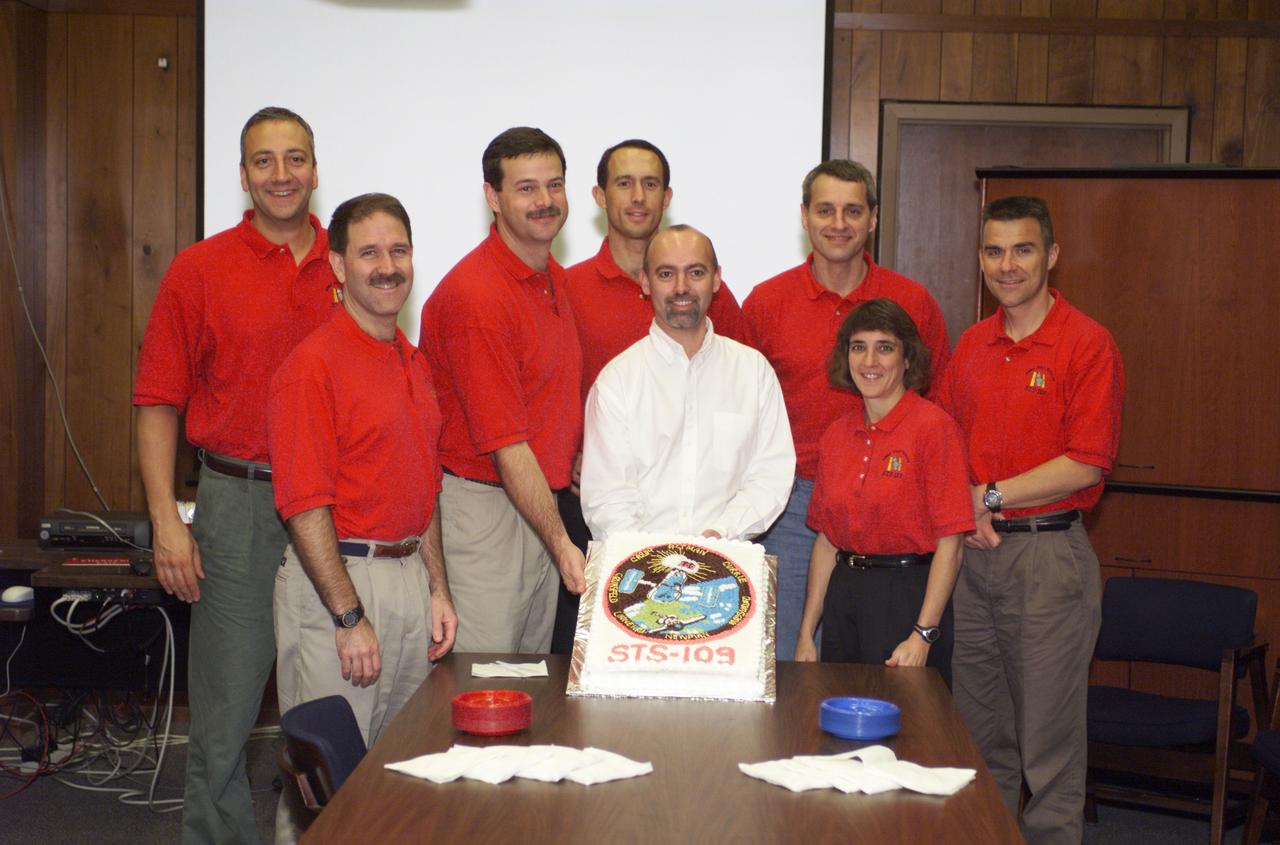 JSC2001-E-44845 (December 2001) --- The STS-109 crew members, along with David Steward (center) of the United Space Alliance (USA), pause from their mission training for a cake cutting ceremony in the Jake Garn Simulation and Training Facility at the Johnson Space Center (JSC). From left to right are astronauts Michael J. Massimino, John M. Grunsfeld, Scott D. Altman, James H. Newman, Richard M. Linnehan, Nancy J. Currie, and Duane G. Carey. Altman and Carey, are mission commander and pilot, respectively. Grunsfeld is payload commander, with the others serving as mission specialists.