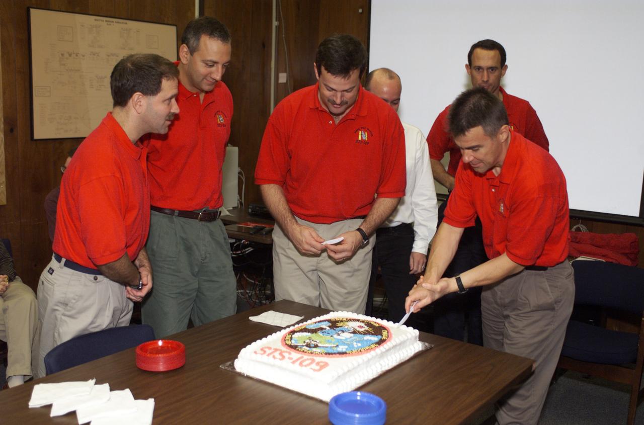 JSC2001-E-44846 (December 2001) --- The STS-109 crew members pause from their mission training for a cake cutting ceremony in the Jake Garn Simulation and Training Facility at the Johnson Space Center (JSC). From left to right are astronauts John M. Grunsfeld, Michael J. Massimino, Scott D. Altman, and Duane G. Carey, James H. Newman; along with David Steward of the United Space Alliance (USA). Altman and Carey are mission commander and pilot, respectively. Grunsfeld is payload commander, with the others serving as mission specialists. Astronauts Nancy J. Currie and Richard M. Linnehan are out of frame.
