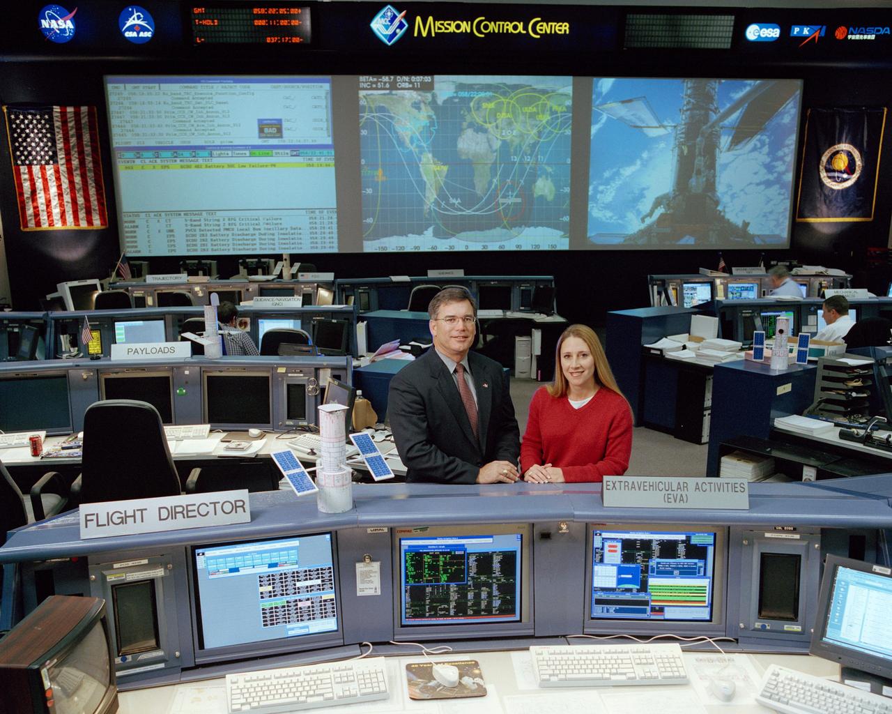 JSC2002-00546 (February 2002) --- Bryan P. Austin, lead flight director for STS-109, and Dana Weigel, lead EVA officer, pose near their respective consoles in the Shuttle Flight Control Room of the Johnson Space Center's Mission Control Center.