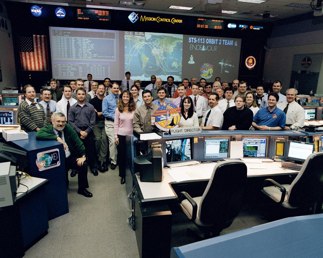 JSC2002-02106 (27 November 2002) --- The members of the STS-113 Orbit 2 Team pose for a group portrait in the shuttle flight control room (WFCR) in Houston&#0146;s Mission Control Center (MCC). Flight Director John Curry stands to the left of the STS-113 mission logo and astronaut Lisa M. Nowak, spacecraft communicator (CAPCOM), stands to the left of Curry.