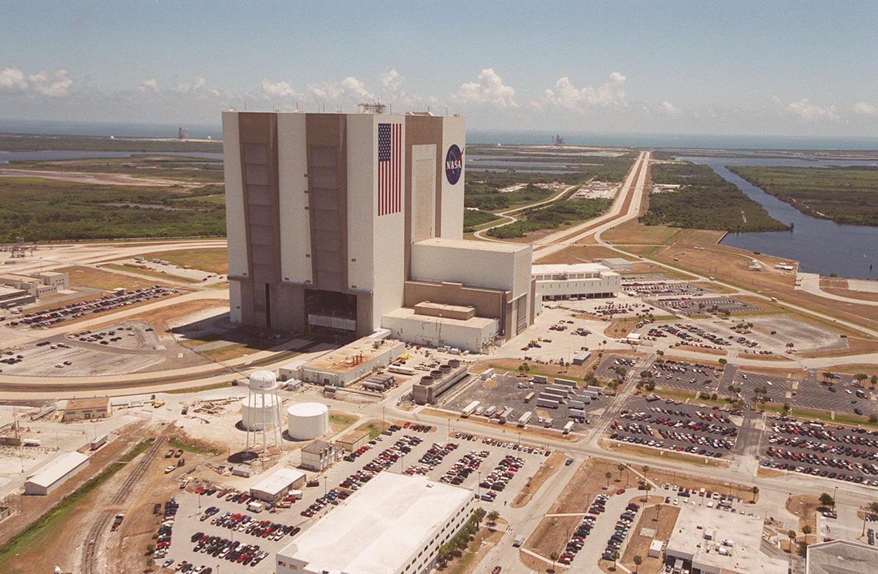 This aerial photo captures many of the facilities involved in Space Shuttle launches. At center is the Vehicle Assembly Building (VAB), with the Launch Control Center at its right. The curved road on the left in the photo is the newly restored crawlerway leading into the VAB high bay 2, where a mobile launcher platform/crawler-transporter sits. The road restoration and high bay 2 are part of KSC's Safe Haven project, enabling the storage of orbiters during severe weather. The crawlerway also extends from the east side out to the two launch pads, one visible close to the road on the left and one to the left of the VAB. In the distance is the Atlantic Ocean. To the right of the crawlerway is the turn basin, into which ships tow the barge for offloading new external tanks from Louisiana. 