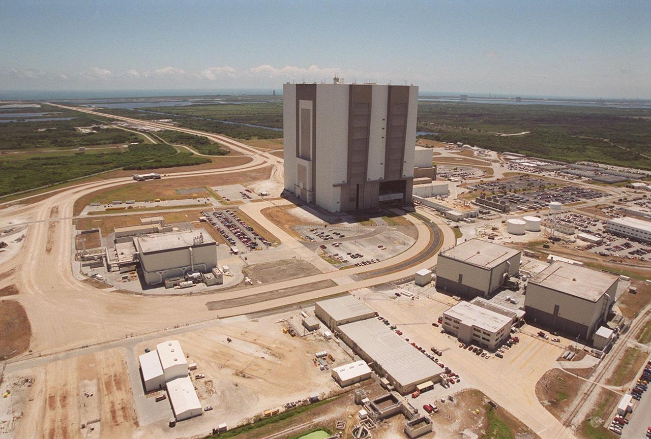 This aerial photo captures many of the facilities involved in Space Shuttle processing. At center is the Vehicle Assembly Building (VAB). The curved road is the newly restored crawlerway leading into the VAB high bay 2. The road restoration and high bay 2 are part of KSC's Safe Haven project, enabling the storage of orbiters during severe weather. The road circles around the Orbiter Processing Facility 3 (OPF-3) at left. OPF1 and OPF-2 are on the right below the curving road. East of the VAB, the crawlerway also extends from high bays 1 and 3 to the two Shuttle launch pads. 