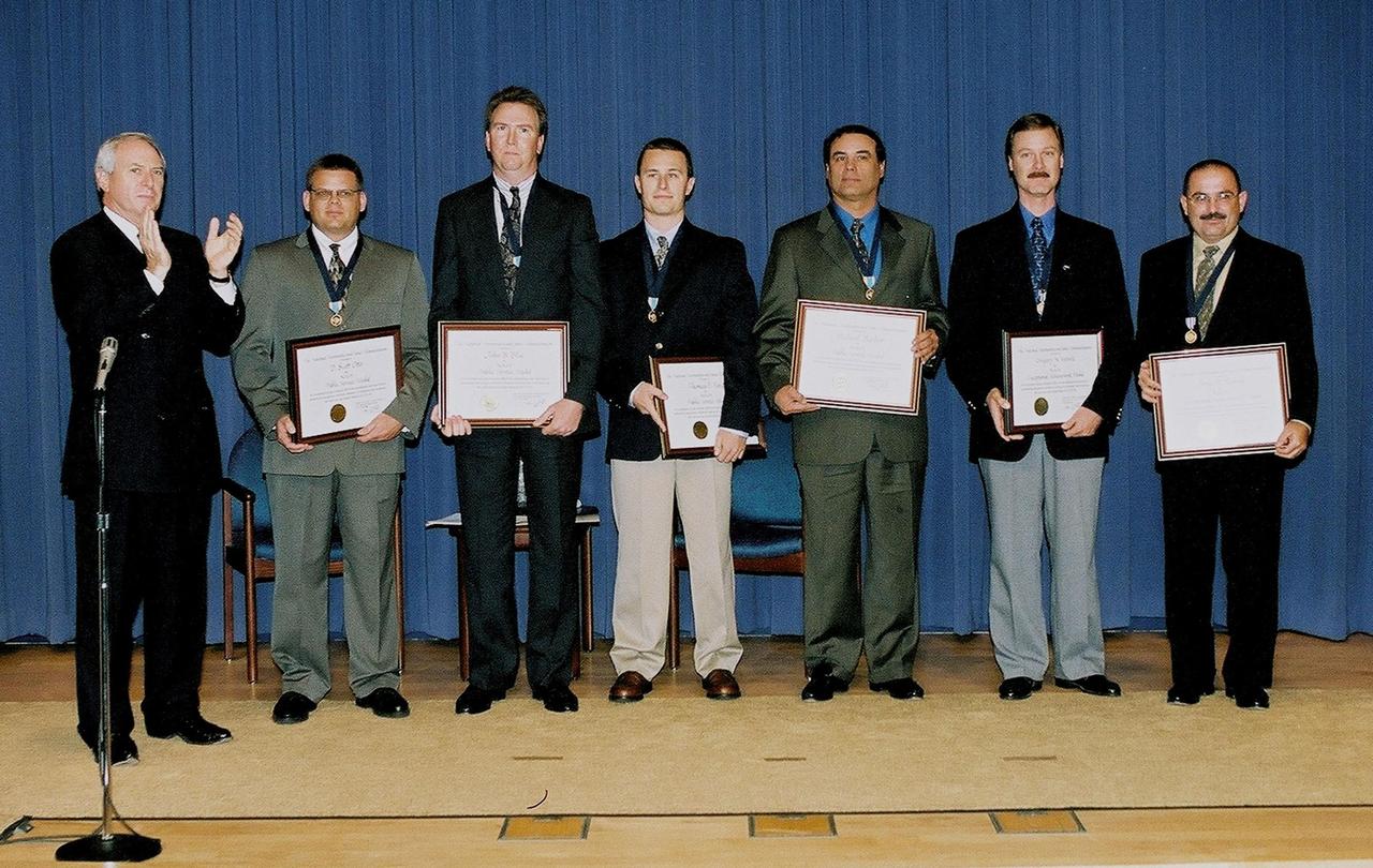 NASA Administrator Daniel Goldin (left) applauds the Space Shuttle ice and debris inspection team who were recognized for their keen safety observations prior to the launch of Space Shuttle Discovery. Standing next to Goldin are (left to right) D. Scott Otto, with Lockheed Martin Space Services Company; John B. Blue, Thomas F. Ford and Michael Barber, with United Space Alliance; Gregory N. Katnik and Jorge E. Rivera, with NASA. Katnick and Rivera received the agency’s Exceptional Achievement Medal; Barber, Blue, Ford and Otto received the NASA Public Service Medal. While scanning the launch pad before launch, the team found a stray 4-inch pin near the Shuttle’s external fuel tank that could have caused damage during launch. Discovery was safely launched the next day, on Oct. 11