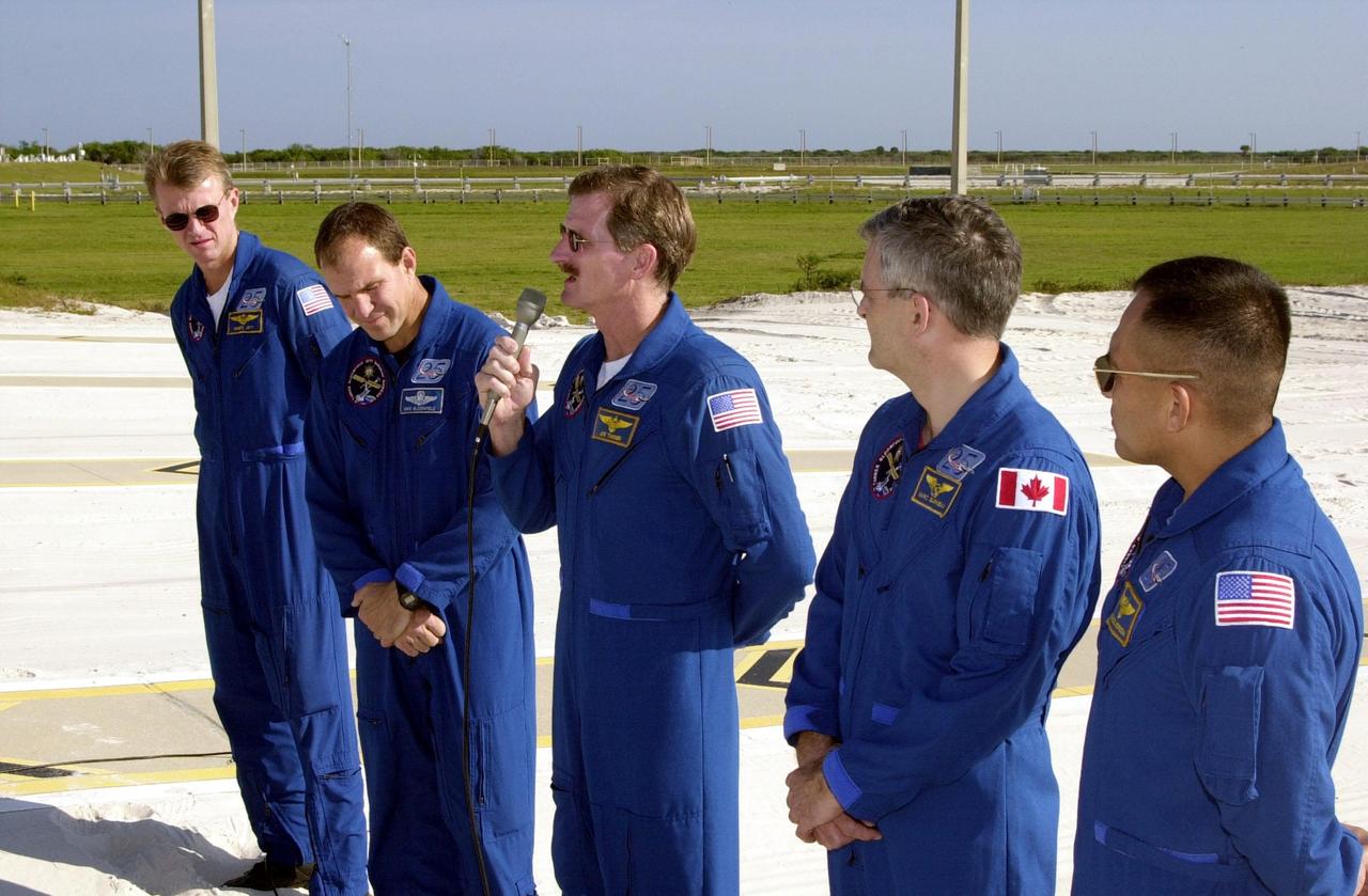 KENNEDY SPACE CENTER, Fla. -- From the slidewire landing zone at Launch Pad 39B, STS-97 Mission Specialist Joe Tanner (center, with microphone) speaks to the press about his extravehicular activity (EVA) during the mission. With him are the rest of the crew, Commander Brent Jett and Pilot Mike Bloomfield on the left and Mission Specialists Marc Garneau and Carlos Noriega on the right. The crew is at KSC to take part in Terminal Countdown Demonstration Test activities that include emergency egress training, familiarization with the payload, and a simulated launch countdown. Visible in the background are the solid rocket booster and external tank on Space Shuttle Endeavour. Mission STS-97is the sixth construction flight to the International Space Station. Its payload includes the P6 Integrated Truss Structure and a photovoltaic (PV) module, with giant solar arrays that will provide power to the Station. The mission includes two spacewalks to complete the solar array connections. STS-97 is scheduled to launch Nov. 30 at about 10:05 p.m. EST