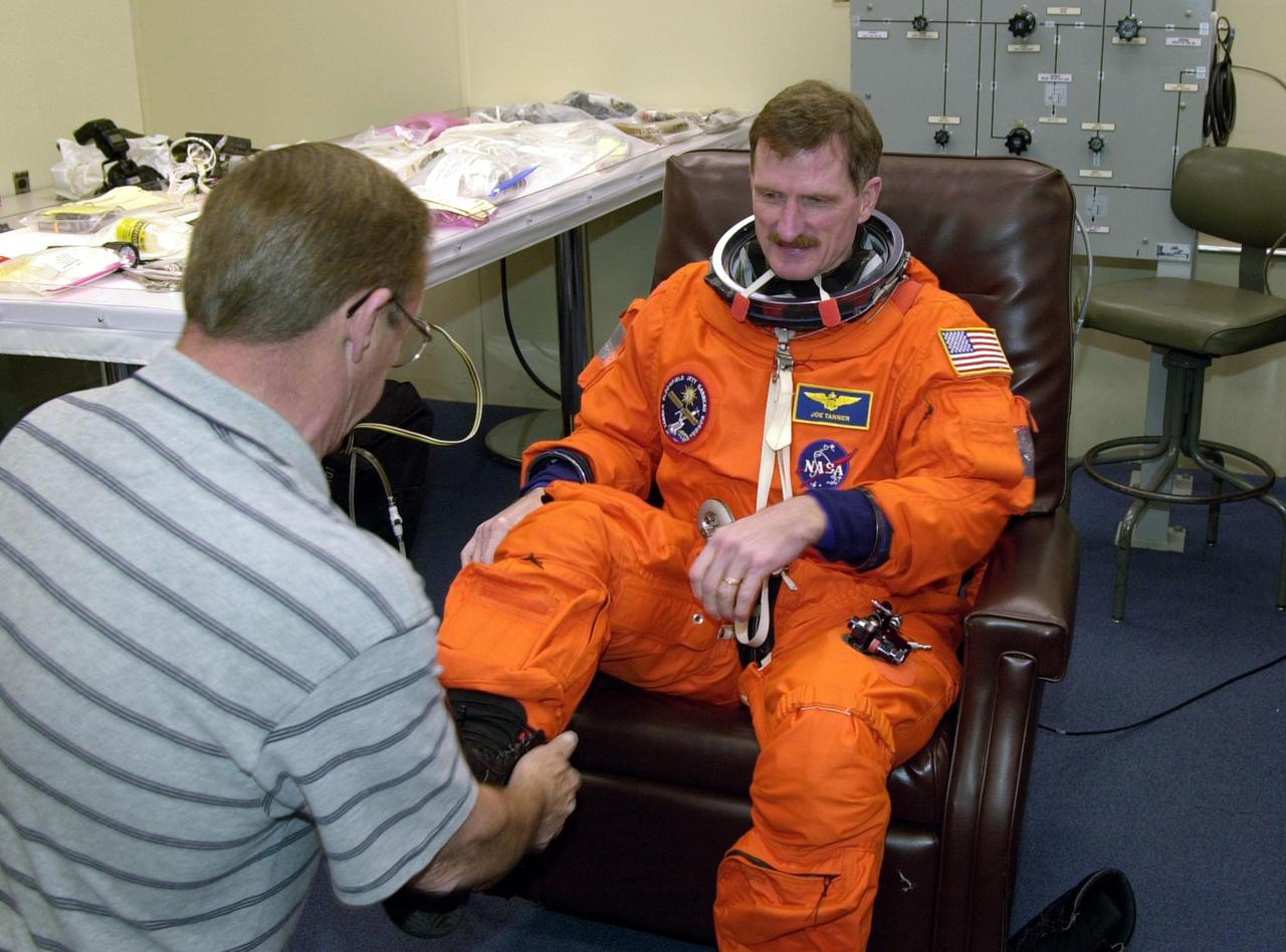 STS-97 Mission Specialist Joseph Tanner gets help with his boots from suit technician Erin Canlon during check pre-pack and fit check. Mission STS-97 is the sixth construction flight to the International Space Station. Its payload includes the P6 Integrated Truss Structure and a photovoltaic (PV) module, with giant solar arrays that will provide power to the Station. The mission includes two spacewalks to complete the solar array connections. STS-97 is scheduled to launch Nov. 30 at about 10:06 p.m. EST