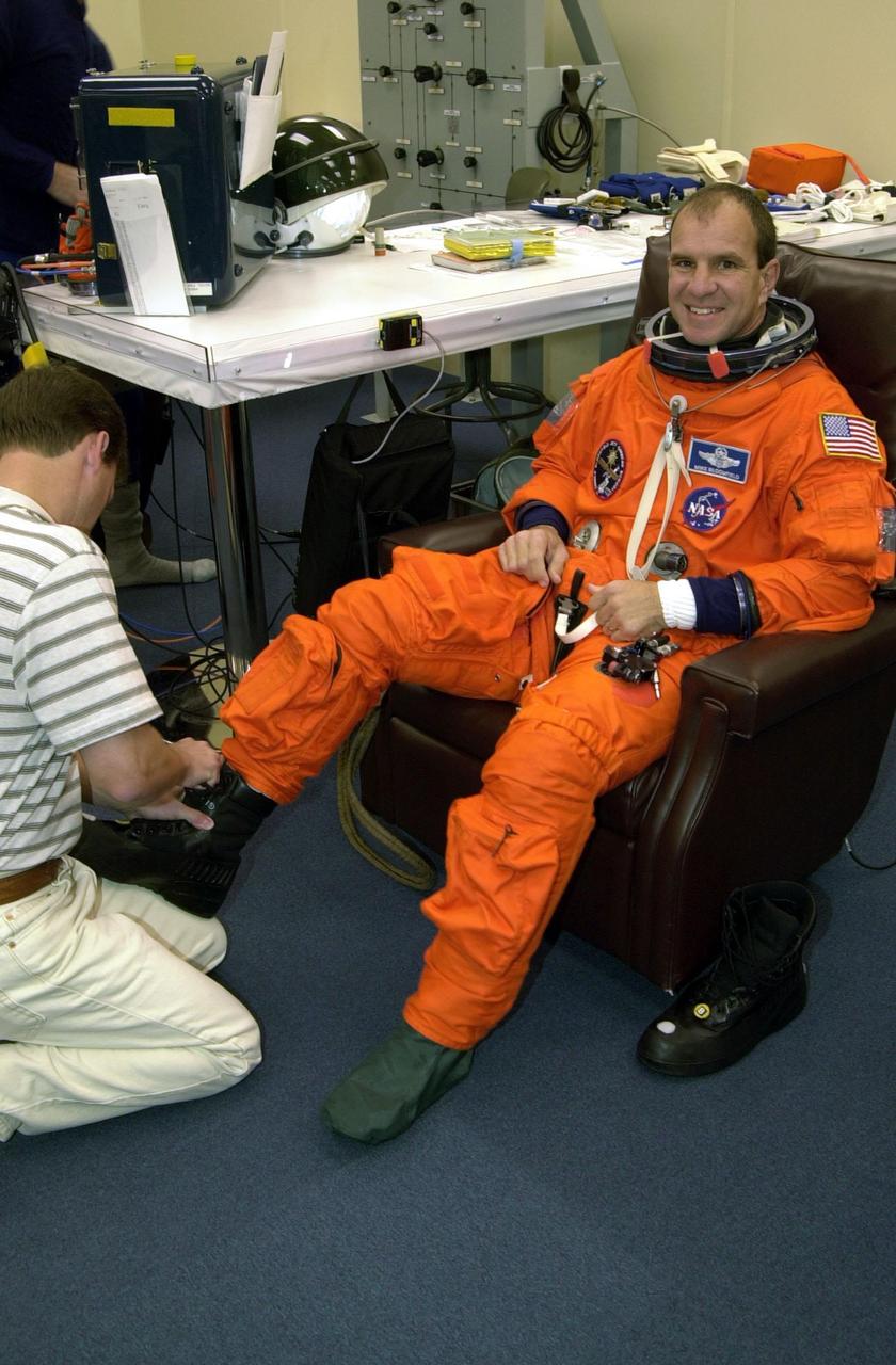 STS-97 Pilot Michael Bloomfield gets help with his boots from suit technician Steve Clendenin during pre-pack and fit check. Mission STS-97 is the sixth construction flight to the International Space Station. Its payload includes the P6 Integrated Truss Structure and a photovoltaic (PV) module, with giant solar arrays that will provide power to the Station. The mission includes two spacewalks to complete the solar array connections. STS-97 is scheduled to launch Nov. 30 at about 10:06 p.m. EST