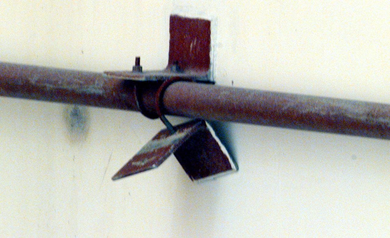 A close-up reveals the loose bracket, observed hanging down from the side of the White Room at Launch Pad 39B, that delayed loading of Endeavour's external tank by several hours to allow technicians to remove it. A "U" bolt connects the bracket to a fire suppression water line attached to the exterior of the White Room. The loose bolt could have possibly created a debris hazard