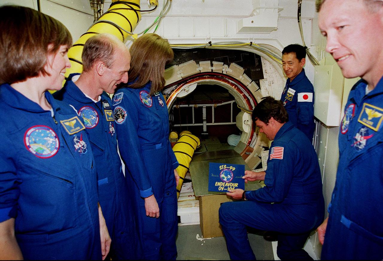Inside the White Room attached to the Fixed Service Structure on Launch Pad 39A, STS-99 Commander Kevin Kregel gets ready to place a sign identifying the mission at the entrance to the orbiter Endeavour. Other crew members gathered around are (left to right) Mission Specialists Janice Voss (Ph.D.), Gerhard Thiele, Janet Lynn Kavandi (Ph.D.) and Mamoru Mohri (behind Kregel), and Pilot Dominic Gorie (at right). Thiele is with the European Space Agency and Mohri is with the National Space Development Agency (NASDA) of Japan. The crew are taking part in Terminal Countdown Demonstration Test activities, which provide them with simulated countdown exercises, emergency egress training, and opportunities to inspect the mission payloads in the orbiter's payload bay. STS-99 is the Shuttle Radar Topography Mission, which will chart a new course, using two antennae and a 200-foot-long section of space station-derived mast protruding from the payload bay to produce unrivaled 3-D images of the Earth's surface. The result of the Shuttle Radar Topography Mission could be close to 1 trillion measurements of the Earth's topography. Besides contributing to the production of better maps, these measurements could lead to improved water drainage modeling, more realistic flight simulators, better locations for cell phone towers, and enhanced navigation safety. Launch of Endeavour on the 11-day mission is scheduled for Jan. 31 at 12:47 p.m. EST