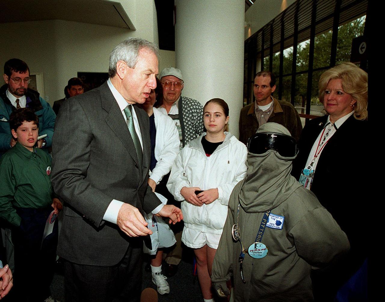 NASA Administrator Dan Goldin (center) talks to 10-year-old Jonathan Pierce (right), who is garbed in a protective cooling suit designed by NASA. In the background, between them, are Jonathan's mother, Penny; his grandfather, John Janocka; and his sister, Jaimie. At left is Mrs. Goldin. Jonathan suffers from erythropoietic protoporphyria, a rare condition that makes his body unable to withstand ultraviolet rays. The suit allows him to be outside during the day, which would otherwise be impossible. Jonathan's trip was funded by the Make-A-Wish Foundation and included a visit to Disney World. He and his family were among a dozen VIPs at KSC to view the launch of STS-99