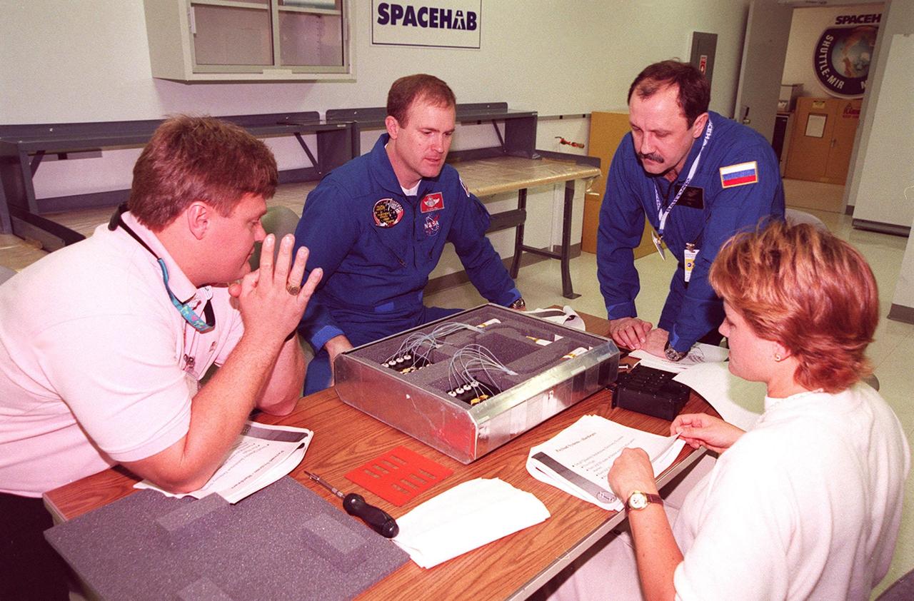 KENNEDY SPACE CENTER, FLA. -- At SPACEHAB, in Cape Canaveral, Fla., members of the STS-101 crew take part in Crew Equipment Interface Test (CEIT) activities, learning about some of the equipment they will be working with on their mission to the International Space Station. Commander James Halsell and Mission Specialist Yuri Usachev of Russia look over a biotube precursor in front of them with (left) Dan Shultz of NASA's Flight Experiments Mission Management Office and (right) April Boody of Bionetics. Other members of the crew (not shown) taking part in the CEIT are Pilot Scott Horowitz and Mission Specialists Mary Ellen Weber, James Voss, Jeffrey Williams and Susan Helms. The crew will be responsible for preparing the Space Station for the arrival of the Zvezda Service Module, expected to be launched by Russia in July 2000. Also, the crew will conduct one space walk to perform maintenance on the Space Station and deliver logistics and supplies. This will be the third assembly flight for the Space Station. STS-101 is scheduled to launch no earlier than April 13 from Launch Pad 39A