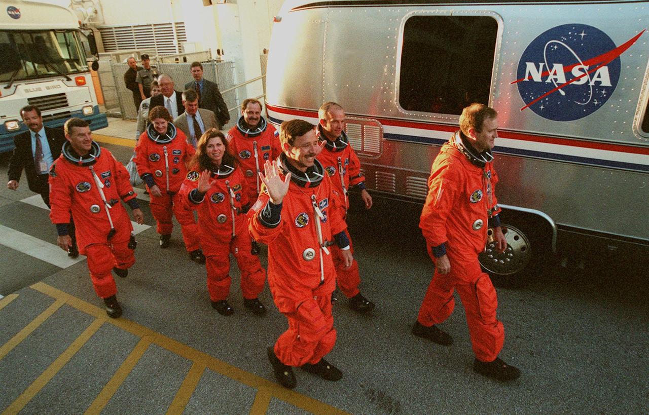 The STS-101 crew wave at onlookers as they walk from the Operations and Checkout Building to the Astrovan, which will take them to Space Shuttle Atlantis on Launch Pad 39A for a simulated countdown exercise. Leading the way are (left) Pilot Scott J. "Doc" Horowitz and (right) Commander James D. Halsell Jr. In the second row are Mission Specialists (left) Mary Ellen Weber and (right) Jeffrey N. Williams. In the third row are Mission Specialists (left) James Voss, (waving) Susan J. Helms, and (right) Yury Usachev of Russia. The dress rehearsal for launch is part of Terminal Countdown Demonstration Test (TCDT) activities that include emergency egress training and familiarization with the payload. During their mission to the International Space Station, the STS-101 crew will be delivering logistics and supplies, plus preparing the Station for the arrival of the Zvezda Service Module, expected to be launched by Russia in July 2000. Also, the crew will conduct one space walk to perform maintenance on the Space Station. This will be the third assembly flight for the Space Station. STS-101 is scheduled to launch April 24 at 4:15 p.m. from Launch Pad 39A