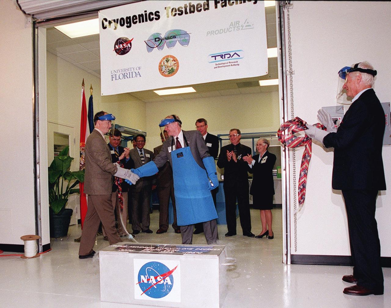 Center Director Roy Bridges (center) is congratulated for the successful breaking of the ceremonial "ribbon" and the opening of the new Cryogenic Testbed Facility. Part of the normal ribbon was replaced with plastic tubing and frozen in liquid nitrogen for the event. Bridges hit the tubing with a small hammer to break it. The Cryogenics Testbed was built to provide cryogenics engineering development and testing services to meet the needs of industry. It will also support commercial, government and academic customers for technology development initiatives on the field of cryogenics. The facility is jointly managed by NASA and Dynacs Engineering Co. , NASA/SC's Engineering Development contractor