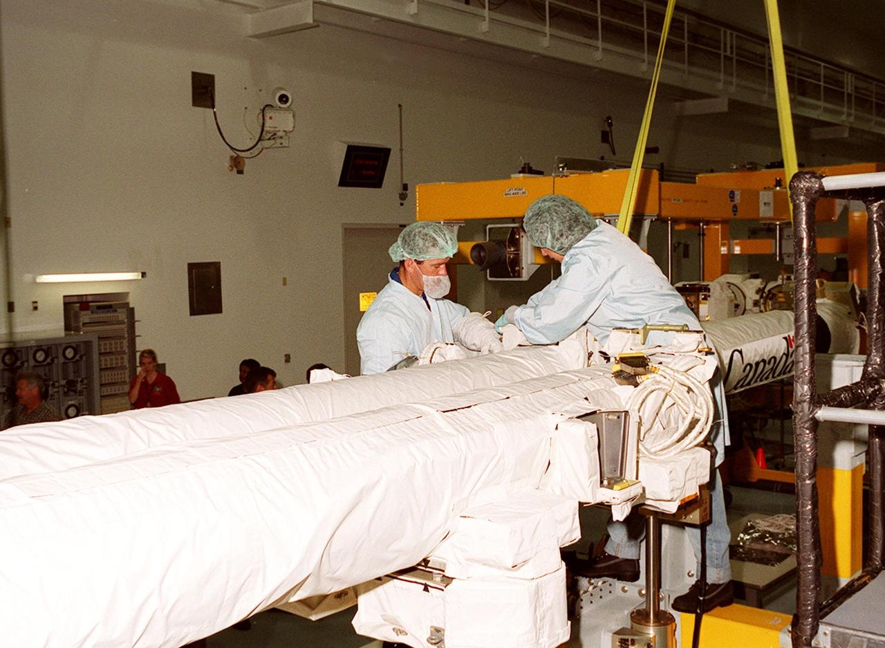 In the Space Station Processing Facility, two workers perform prelaunch processing activities on the Canadian Space Agency's (CSA) Space Station Remote Manipulator System (SSRMS). CSA's first contribution to the International Space Station (ISS), the SSRMS is the primary means of transferring payloads between the orbiter payload bay and the ISS for assembly. The 56-foot-long robotic arm includes two 12-foot booms joined by a hinge. Seven joints on the arm allow highly flexible and precise movement. Latching End Effectors are mounted on each end of the arm for grappling. Video cameras mounted on the booms and end effectors will give astronauts maximum visibility for operations and maintenance tasks on the ISS. The SSRMS is scheduled to be launched aboard Space Shuttle Endeavour on STS-100, currently planned for April 2001