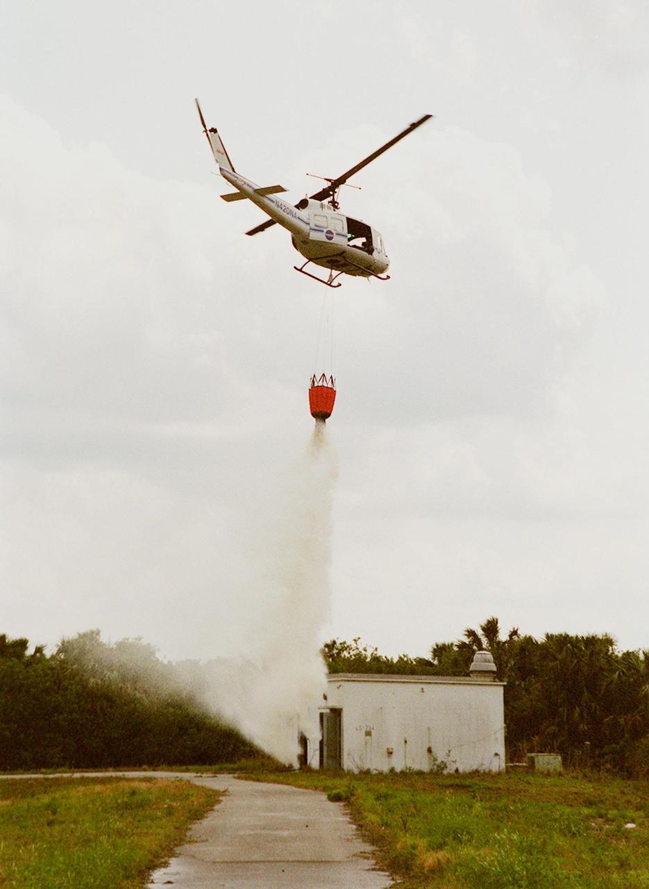 KENNEDY SPACE CENTER, FLA. -- A NASA helicopter releases 324 gallons of water onto a building in a simulated fire control demonstration. The high-impact-resistant flexible plastic bucket will be used for fire protection on property and buildings at Kennedy Space Center. Known as the "Bambi" bucket, it will also support the Fish and Wildlife Service for controlled burns plus any wild fires in the area.
