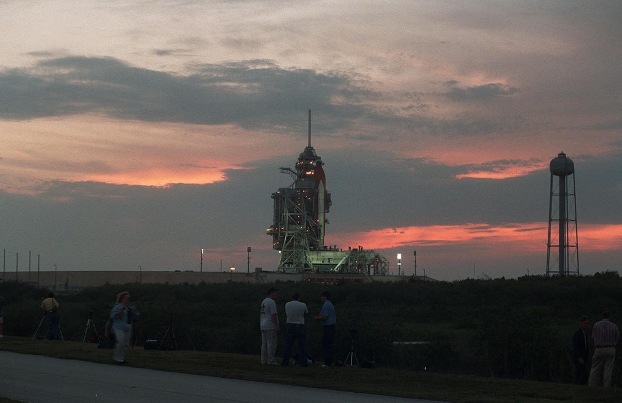 KENNEDY SPACE CENTER, Fla. -- The darkening sky at sunset provides a dramatic backdrop for Space Shuttle Atlantis on Launch Pad 39A. Spectators (bottom) wait for the rollback of the Rotating Service Structure to reveal the orbiter. In the photo only the orange external tank and white solid rocket booster are visible. Atlantis is targeted for liftoff at 4:15 p.m. EDT April 24 on mission STS-101. The mission will take the crew to the International Space Station to deliver logistics and supplies and prepare the Station for the arrival of the Zvezda Service Module, expected to be launched by Russia in July 2000. Also, the crew will conduct one space walk. This will be the third assembly flight to the Space Station