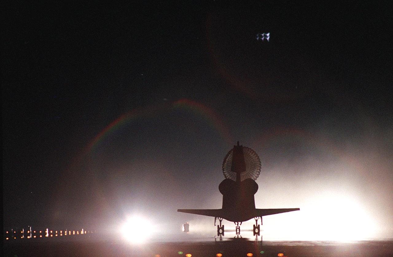 KENNEDY SPACE CENTER, Fla. -- With its drag chute billowing behind, Space Shuttle Atlantis is silhouetted against the bright lights on Runway 15, Shuttle Landing Facility, as it rolls to a stop. Two rainbows appear above the lights. The landing of Atlantis completed the 9-day, 20-hour, 9-minute-long STS-101 mission. At the controls are Commander James D. Halsell Jr. and Pilot Scott “Doc” Horowitz. Also onboard the orbiter are Mission Specialists Mary Ellen Weber, James S. Voss, Jeffrey N. Williams, Susan J. Helms and Yury Usachev of Russia. Main gear touchdown was at 2:20:17 a.m. EDT, landing on orbit 155 of the mission. Nose gear touchdown was at 2:20:30 a.m. EDT, and wheel stop at 2:21:19 a.m. EDT. The crew is returning from the third flight to the International Space Station. This was the 98th flight in the Space Shuttle program and the 21st for Atlantis, also marking the 51st landing at KSC, the 22nd consecutive landing at KSC, the 14th nighttime landing in Shuttle history and the 29th in the last 30 Shuttle flights