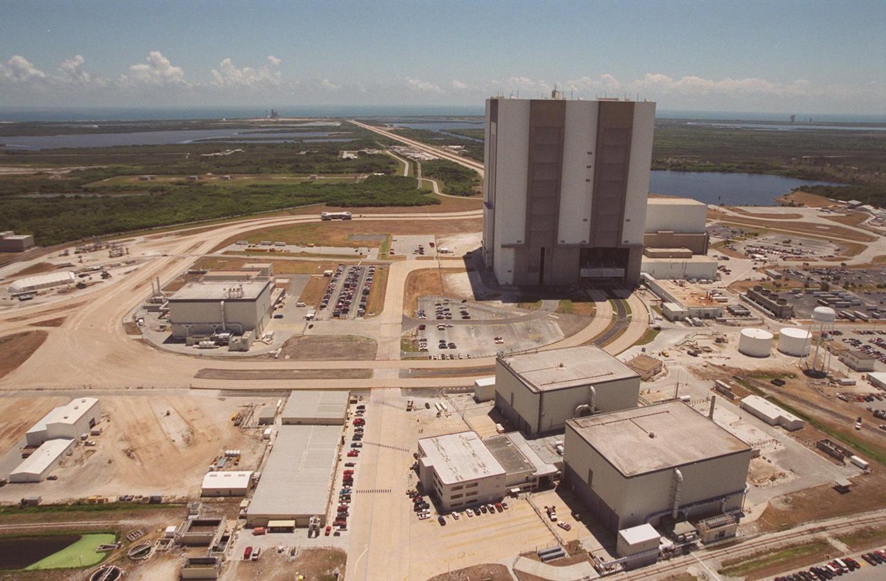 This aerial photo shows the areas recently opened as part of KSC’s Safe Haven project. The curved road in the center is the newly restored crawlerway leading around the Vehicle Assembly Building (VAB) and Orbiter Processing Facility 3 (OPF-3) into the VAB high bay 2 (open on the lower right), where a mobile launcher platform/crawler-transporter currently sits. The Safe Haven project will enable the storage of orbiters during severe weather. OPF1 and OPF-2 are at the lower right. The crawlerway also extends from the east side of the VAB out to the two launch pads. Launch Pad 39A is visible to the left of the crawlerway. In the distance is the Atlantic Ocean. To the right of the VAB is the turn basin, into which ships tow the barge for offloading new external tanks from Louisiana