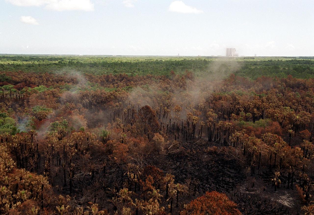Smoke rising from the smoldering brush on Kennedy Space Center illustrates the hazardous fire conditions that exist throughout Central Florida. The 525-foot tall Vehicle Assembly Building is in the background. The site is between Kennedy Parkway North and the Indian River
