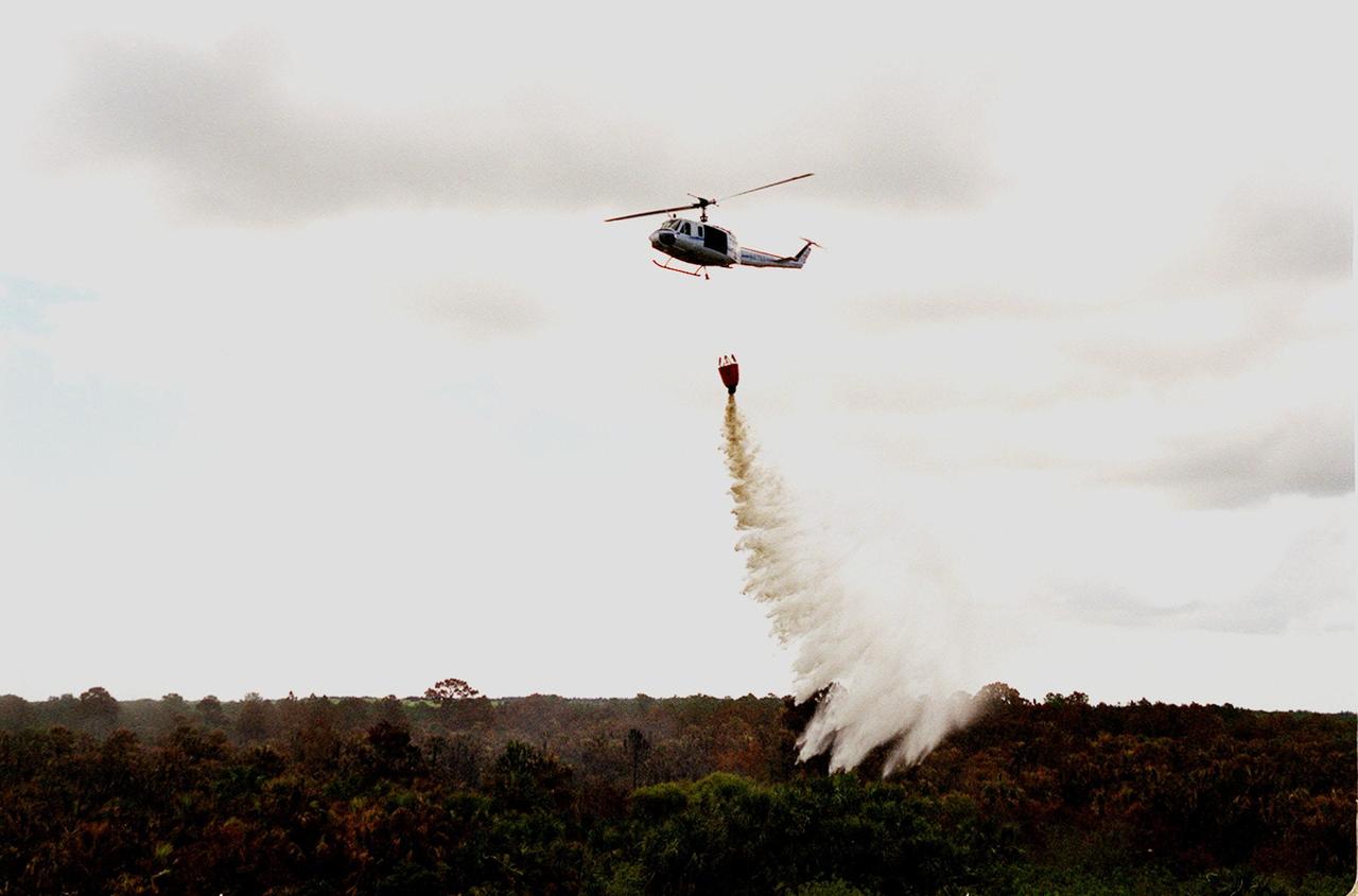 A helicopter dumps water on smoldering brush on Kennedy Space Center. Hazardous fire conditions exist throughout Central Florida. The site is between Kennedy Parkway North and the Indian River