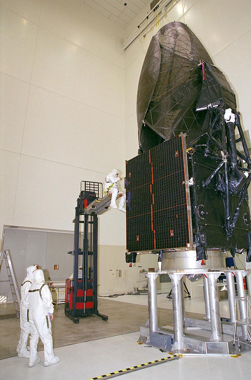 In the Spacecraft Assembly and Encapsulation Facility, a worker (left center) checks out the Tracking and Data Relay Satellite (TDRS-H) after its move to the payload adapter (below). Next step is the encapsulation of the TDRS in the fairing. TDRS is scheduled to be launched June 29 aboard an Atlas IIA/Centaur rocket. One of three satellites (labeled H, I and J) being built in the Hughes Space and Communications Company Integrated Satellite Factory in El Segundo, Calif., the latest TDRS uses an innovative springback antenna design. A pair of 15-foot-diameter, flexible mesh antenna reflectors fold up for launch, then spring back into their original cupped circular shape on orbit. The new satellites will augment the TDRS system’s existing Sand Ku-band frequencies by adding Ka-band capability. TDRS will serve as the sole means of continuous, high-data-rate communication with the space shuttle, with the International Space Station upon its completion, and with dozens of unmanned scientific satellites in low earth orbit