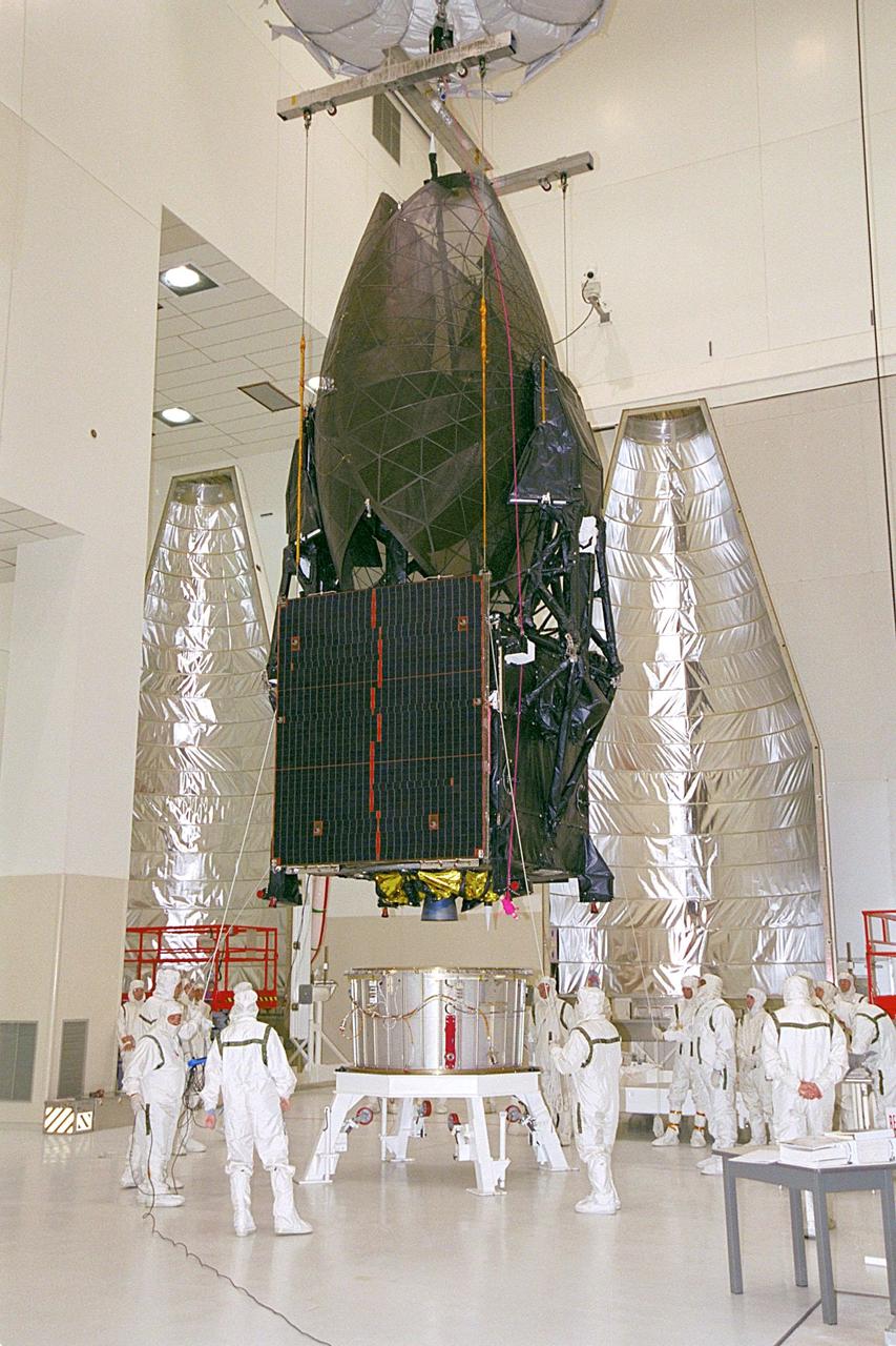 In the Spacecraft Assembly and Encapsulation Facility, overhead cranes lower the Tracking and Data Relay Satellite (TDRS-H) onto a payload adapter. Next step is the encapsulation of the satellite in the fairing behind it (right and left). TDRS is scheduled to be launched June 29 aboard an Atlas IIA/Centaur rocket. One of three satellites (labeled H, I and J) being built in the Hughes Space and Communications Company Integrated Satellite Factory in El Segundo, Calif., the latest TDRS uses an innovative springback antenna design. A pair of 15-foot-diameter, flexible mesh antenna reflectors fold up for launch, then spring back into their original cupped circular shape on orbit. The new satellites will augment the TDRS system’s existing Sand Ku-band frequencies by adding Ka-band capability. TDRS will serve as the sole means of continuous, high-data-rate communication with the space shuttle, with the International Space Station upon its completion, and with dozens of unmanned scientific satellites in low earth orbit