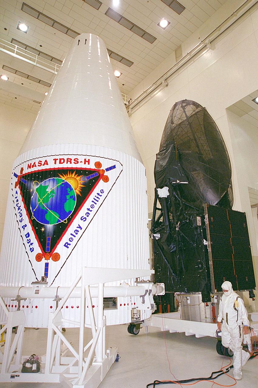 In the Spacecraft Assembly and Encapsulation Facility, the Tracking and Data Relay Satellite (TDRS-H) at right sits while one-half of the fairing (left) is moved closer to it. After encapsulation in the fairing, TDRS will be transported to Launch Pad 36A, Cape Canaveral Air Force Station for launch scheduled June 29 aboard an Atlas IIA/Centaur rocket. One of three satellites (labeled H, I and J) being built in the Hughes Space and Communications Company Integrated Satellite Factory in El Segundo, Calif., the latest TDRS uses an innovative springback antenna design. A pair of 15-foot-diameter, flexible mesh antenna reflectors fold up for launch, then spring back into their original cupped circular shape on orbit. The new satellites will augment the TDRS system’s existing Sand Ku-band frequencies by adding Ka-band capability. TDRS will serve as the sole means of continuous, high-data-rate communication with the space shuttle, with the International Space Station upon its completion, and with dozens of unmanned scientific satellites in low earth orbit