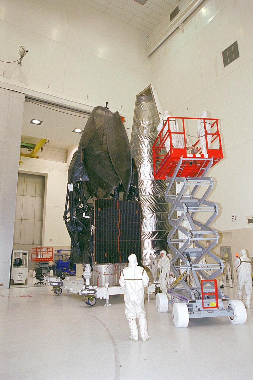 In the Spacecraft Assembly and Encapsulation Facility, the Tracking and Data Relay Satellite (TDRS-H) at left is ready for encapsulation. Workers in an extended platform are moved closer to the fairing at right of the satellite. After encapsulation in the fairing, TDRS will be transported to Launch Pad 36A, Cape Canaveral Air Force Station for launch scheduled June 29 aboard an Atlas IIA/Centaur rocket. One of three satellites (labeled H, I and J) being built in the Hughes Space and Communications Company Integrated Satellite Factory in El Segundo, Calif., the latest TDRS uses an innovative springback antenna design. A pair of 15-foot-diameter, flexible mesh antenna reflectors fold up for launch, then spring back into their original cupped circular shape on orbit. The new satellites will augment the TDRS system’s existing Sand Ku-band frequencies by adding Ka-band capability. TDRS will serve as the sole means of continuous, high-data-rate communication with the space shuttle, with the International Space Station upon its completion, and with dozens of unmanned scientific satellites in low earth orbit