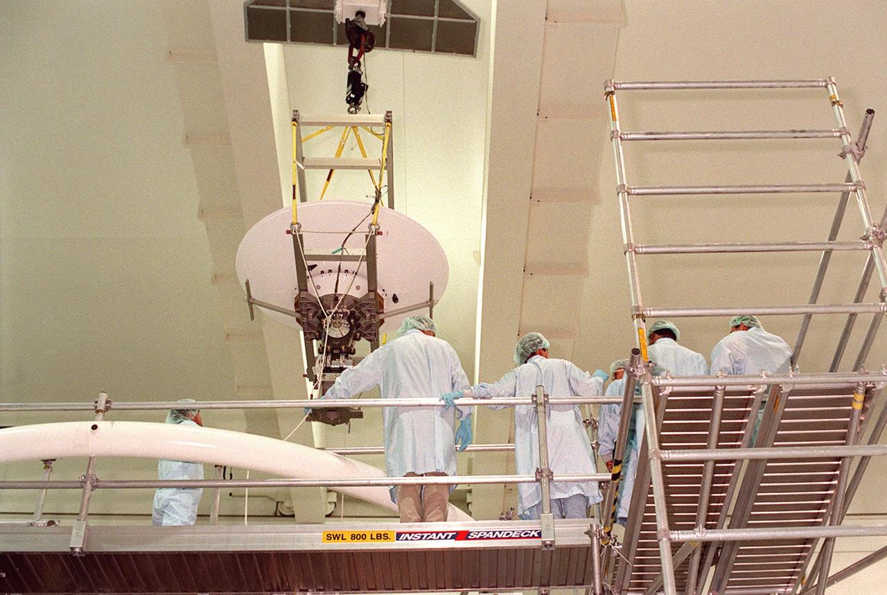 An overhead crane in the Space Shuttle Processing Facility lifts a high-gain antenna over a work platform toward the Integrated Truss Structure (ITS) Z1, to which it will be attached. The Z1, part of the payload on mission STS-92 (flight 3A) to be launched in mid-fall, is an early exterior framework for the International Space Station. It will allow the first U.S. solar arrays, on mission STS-97 (flight 4A), to be temporarily installed on Unity for early power