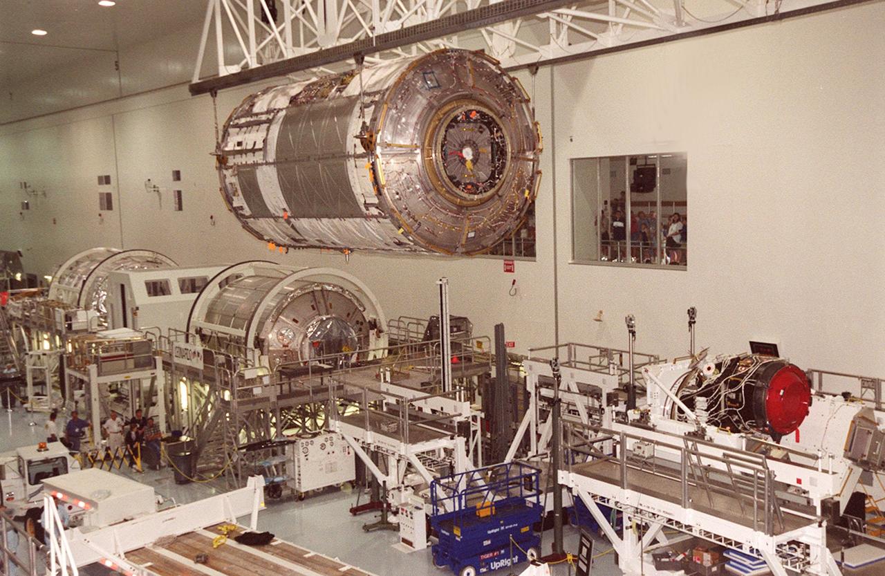 KENNEDY SPACE CENTER, FLA. -- In the Space Station Processing Facility, the U.S. Laboratory Destiny, a component of the International Space Station, glides overhead other hardware while visitors watch from a window (right). On the floor, left to right, are two Multi-Purpose Logistics Modules (MPLMs), Raffaello (far left) and Leonardo, and a Pressurized Mating Adapter-3 (right). Destiny is being moved to a payload canister for transfer to the Operations and Checkout Building where it will be tested in the altitude chamber. Destiny is scheduled to fly on mission STS-98 in early 2001. During the mission, the crew will install the Lab in the Space Station during a series of three space walks. The STS-98 mission will provide the Station with science research facilities and expand its power, life support and control capabilities. The U.S. Lab module continues a long tradition of microgravity materials research, first conducted by Skylab and later Shuttle and Spacelab missions. Destiny is expected to be a major feature in future research, providing facilities for biotechnology, fluid physics, combustion, and life sciences research